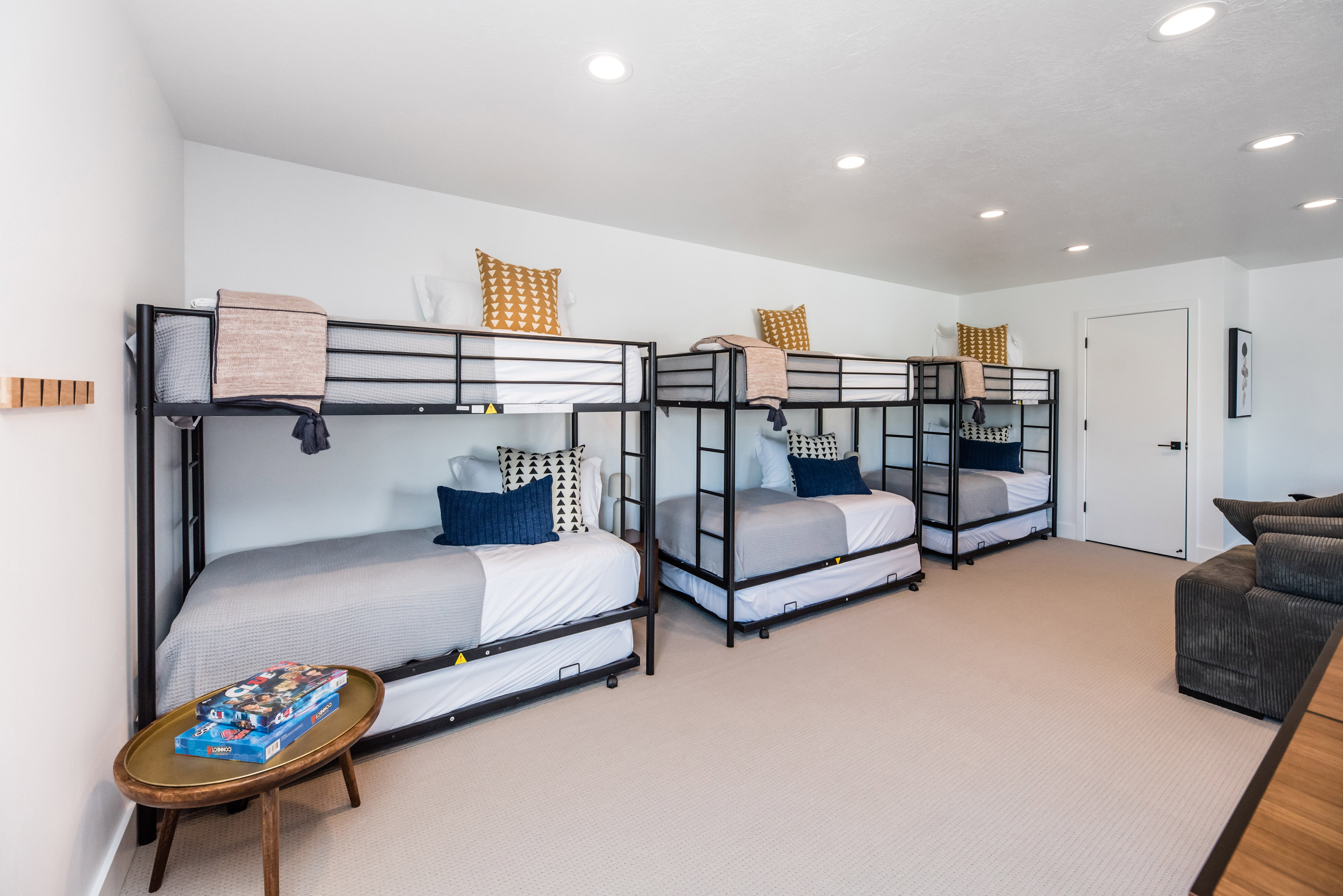 Spacious room featuring three metal-frame bunk beds with trundles, white walls, recessed lighting, and light-colored carpet flooring