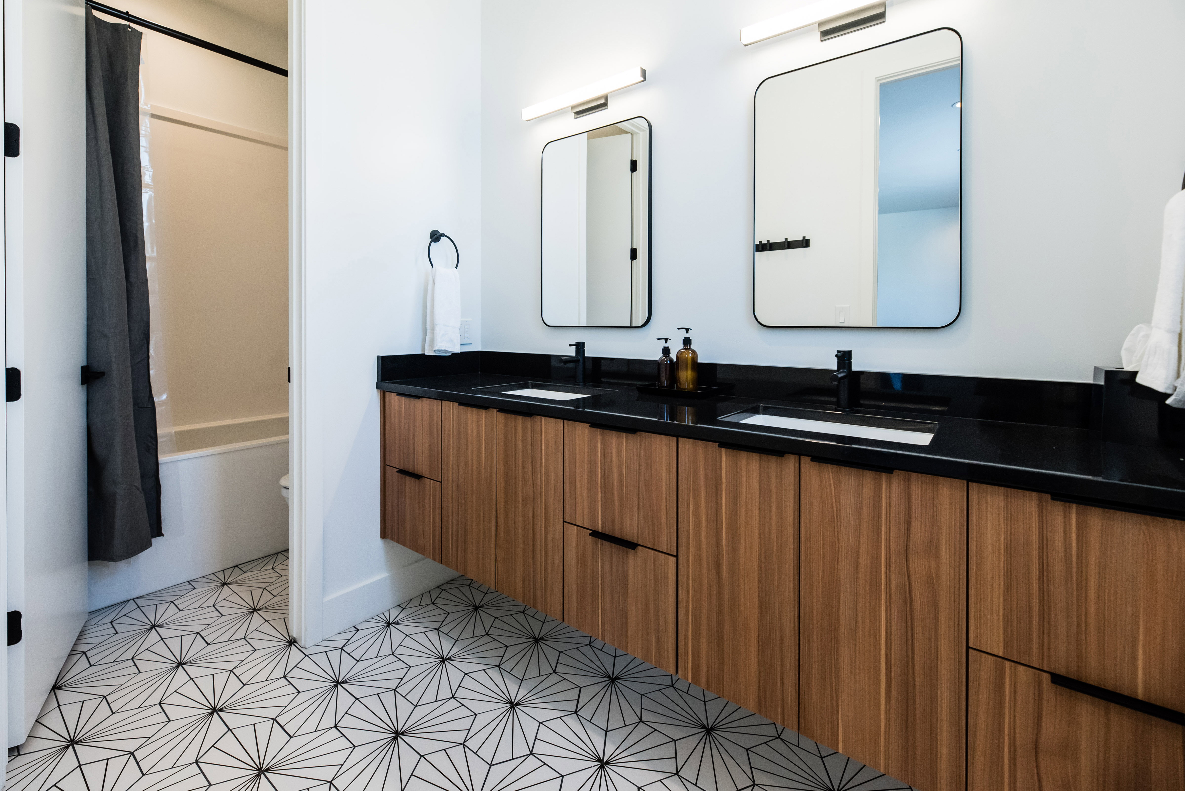 Contemporary bathroom featuring a floating wood-finish double vanity with a dark countertop and integrated sinks