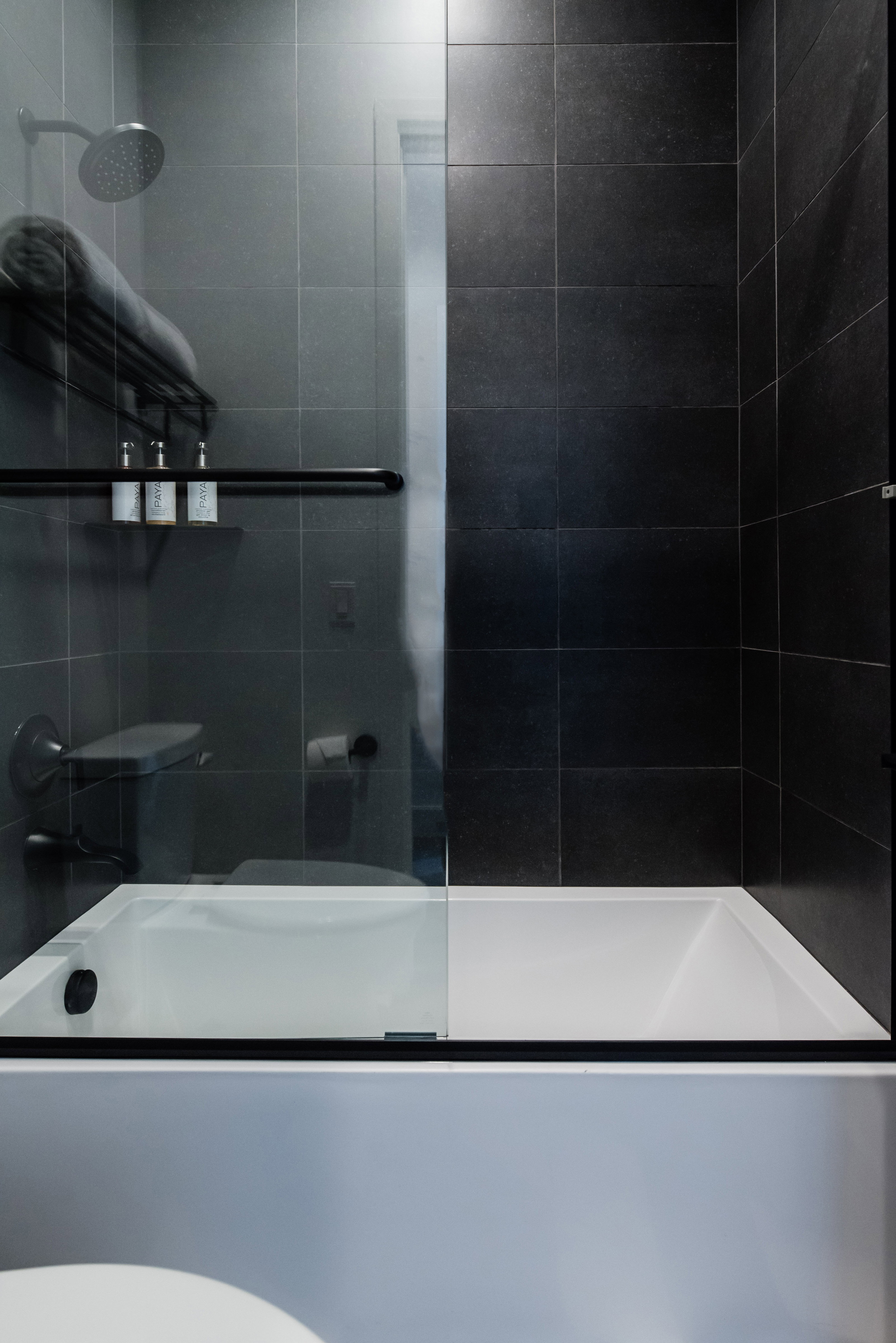 Contemporary bathtub and shower combination featuring dark tile surround