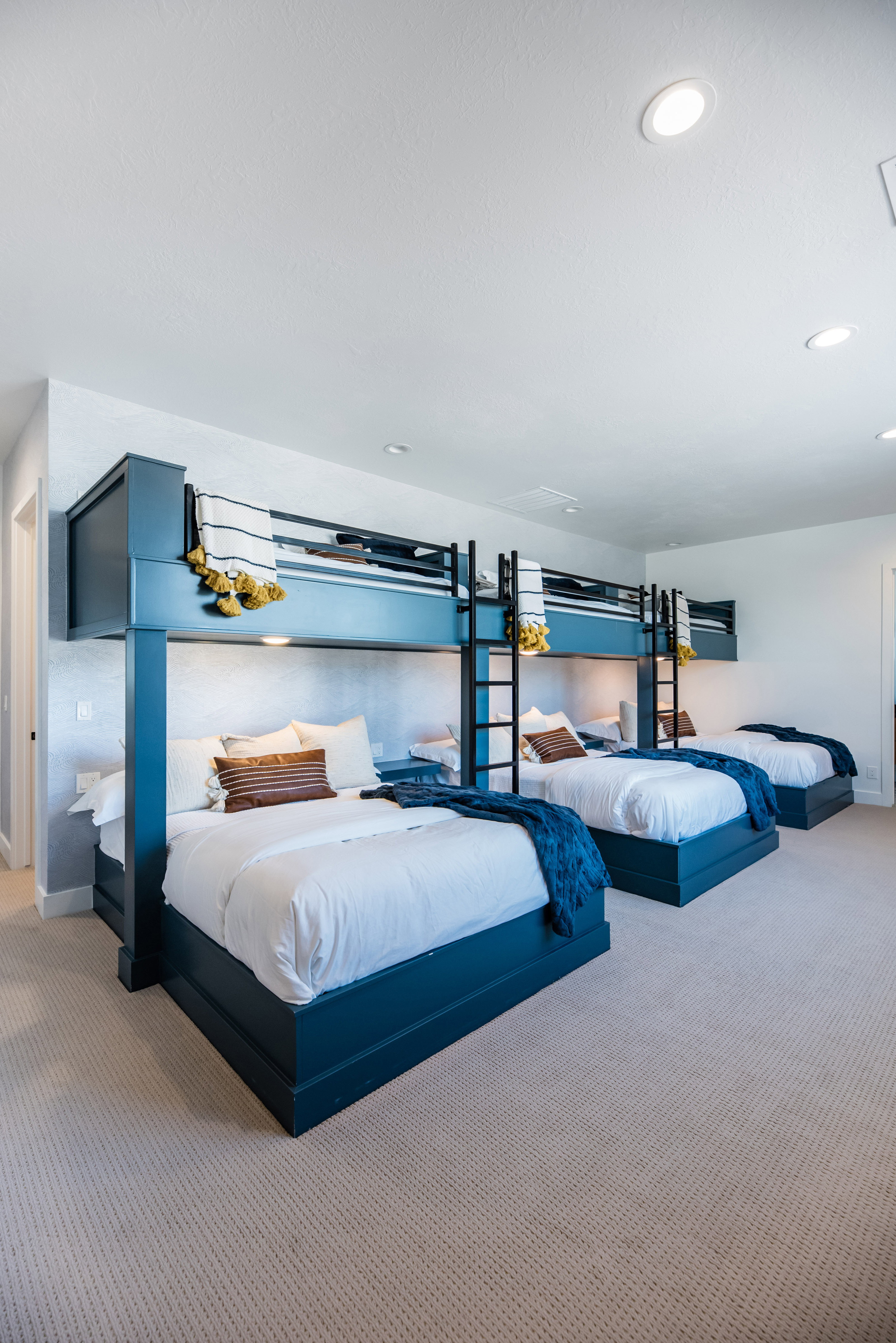 Spacious room featuring three built-in bunk bed structures with integrated ladders, recessed lighting, and light-colored carpeting