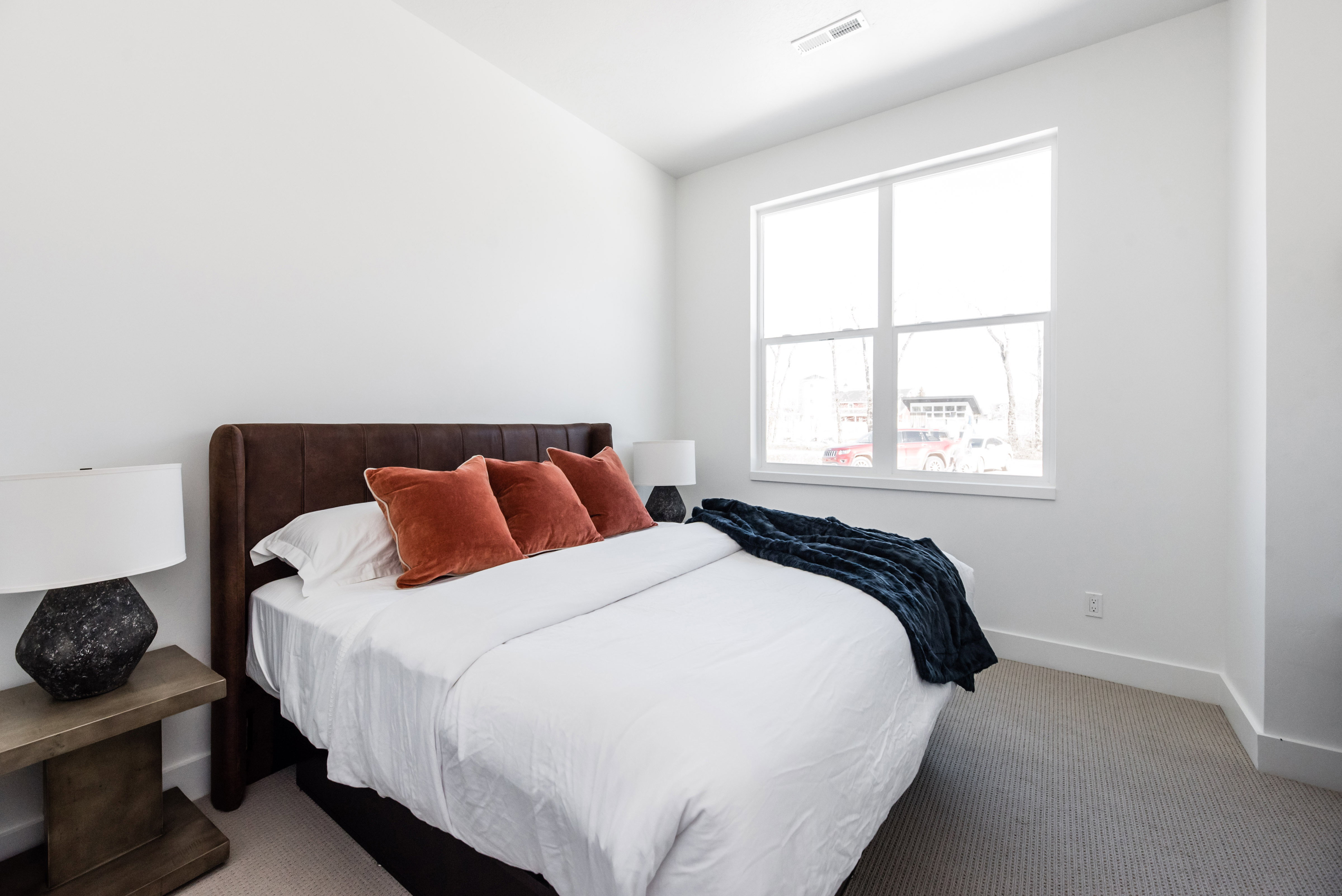 Bright bedroom featuring a large window, neutral wall paint, and gray carpet flooring