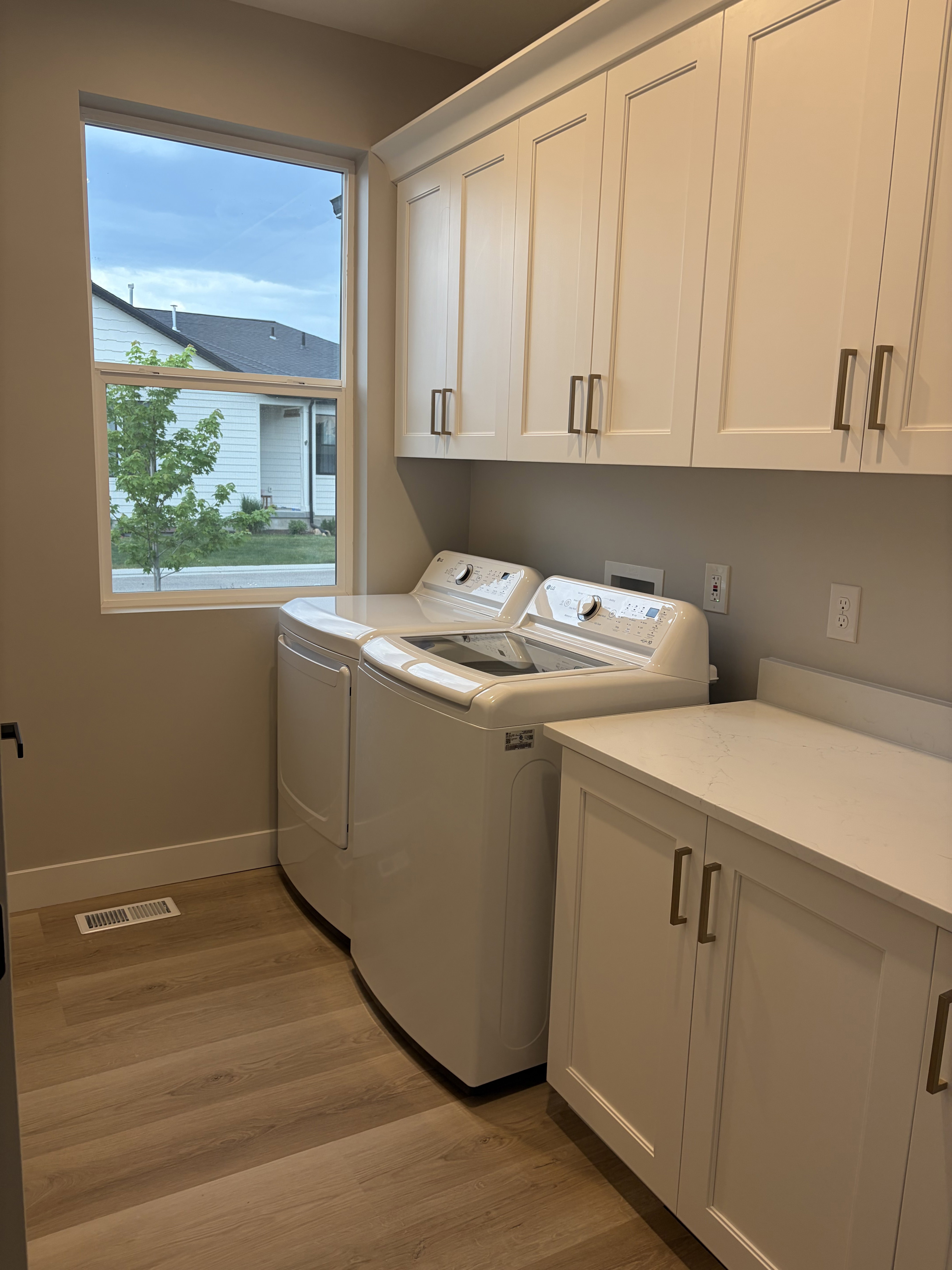 Laundry room featuring white shaker-style cabinetry, a built-in counter, wood-finish flooring, and a large window