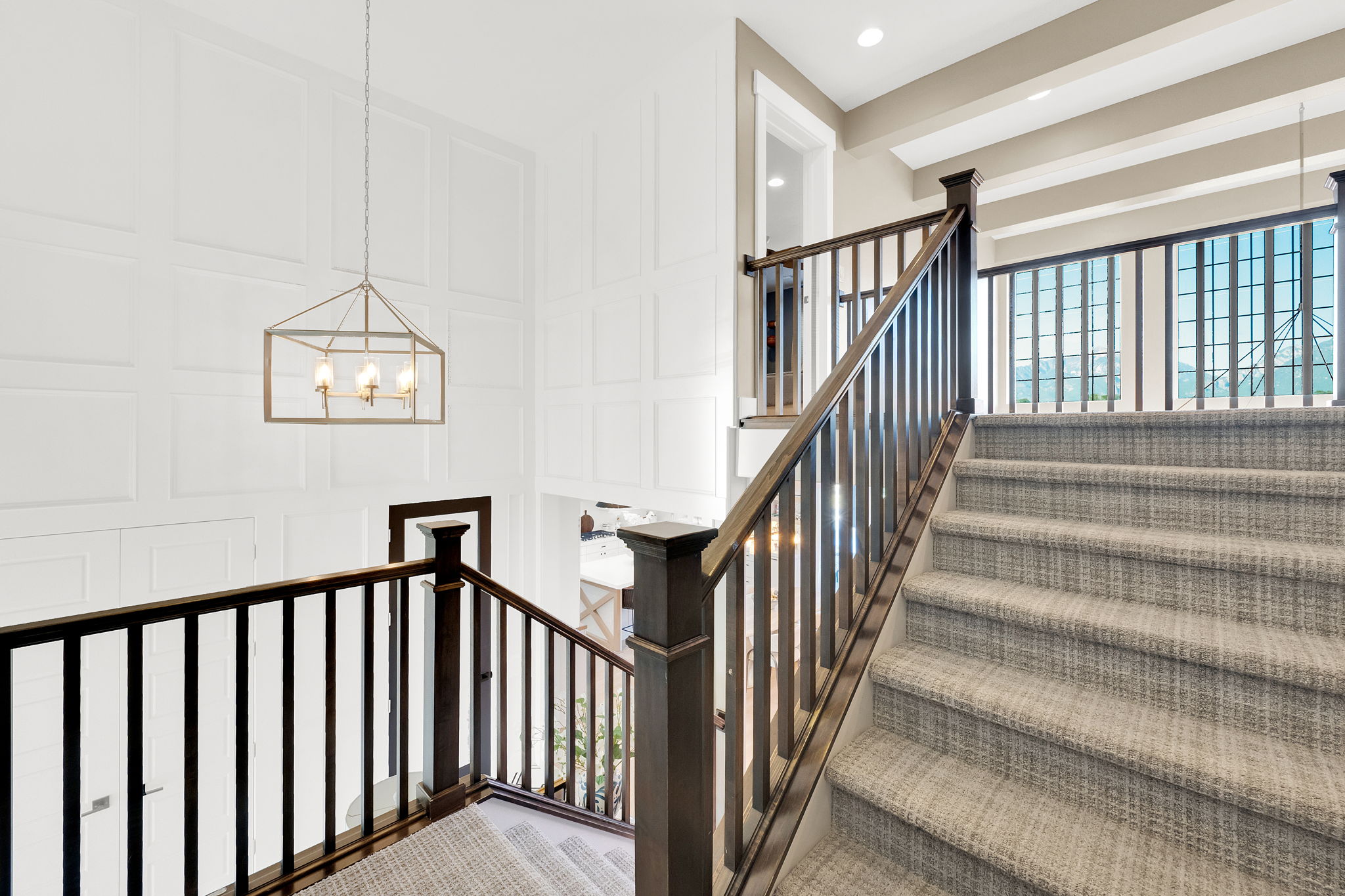 Staircase featuring dark wood handrails, light gray patterned carpeting, and white paneled walls