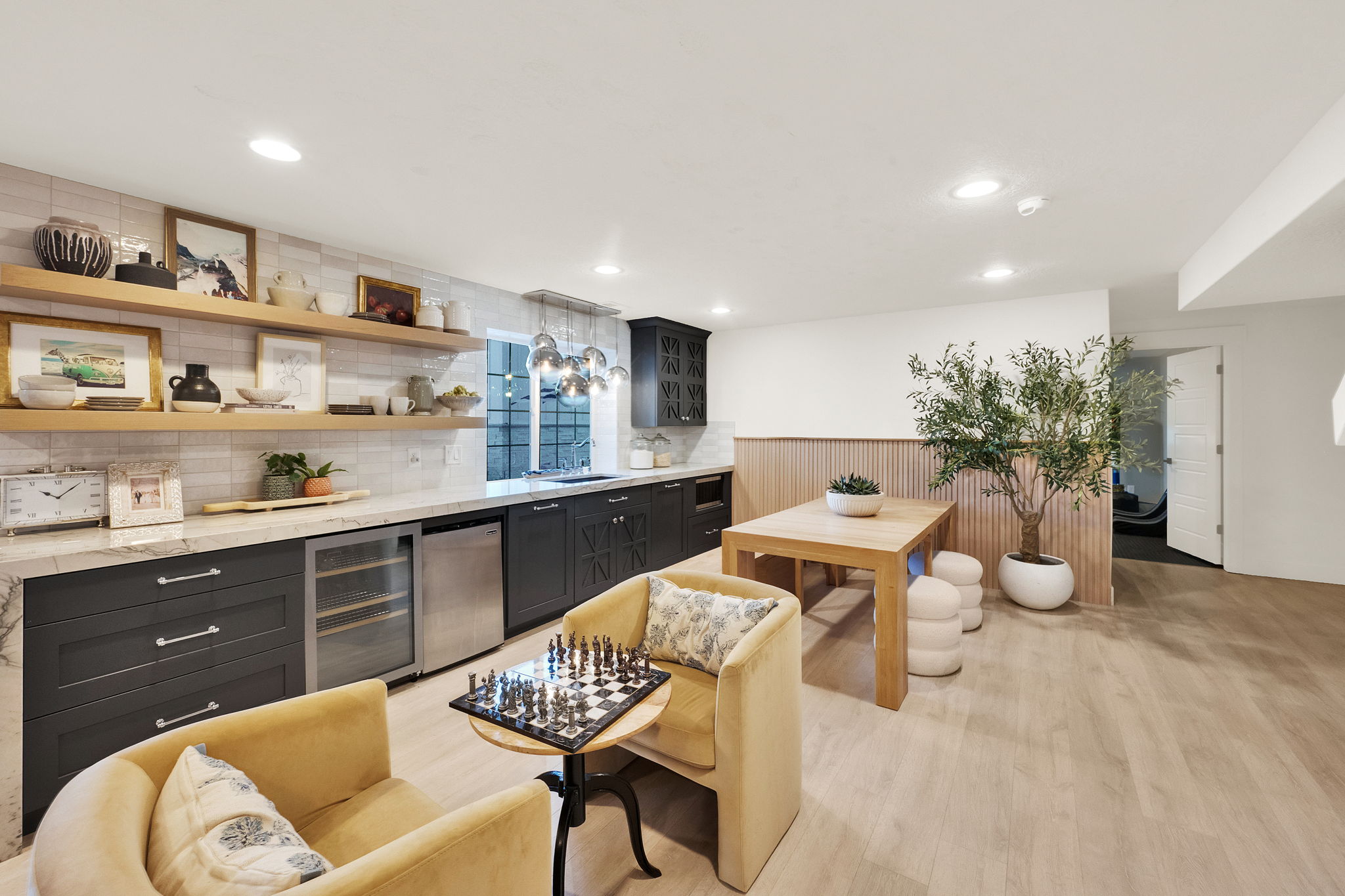 Recessed lighting illuminates a well-appointed kitchen area featuring dark cabinetry, a beverage refrigerator, and a light-toned countertop