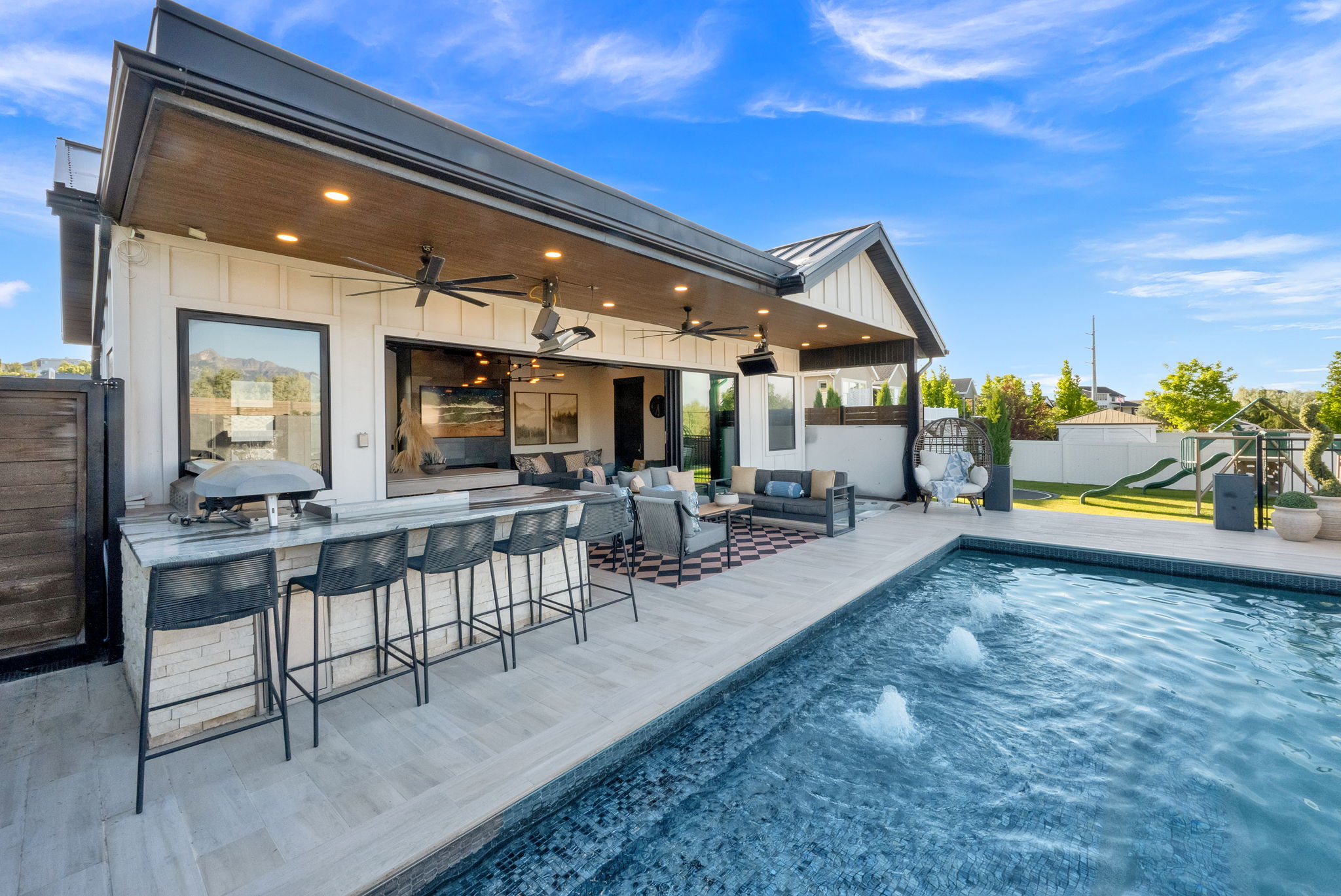 Outdoor living space featuring a swimming pool with water features, an outdoor kitchen with bar seating, and a covered patio with recessed lighting and ceiling fans
