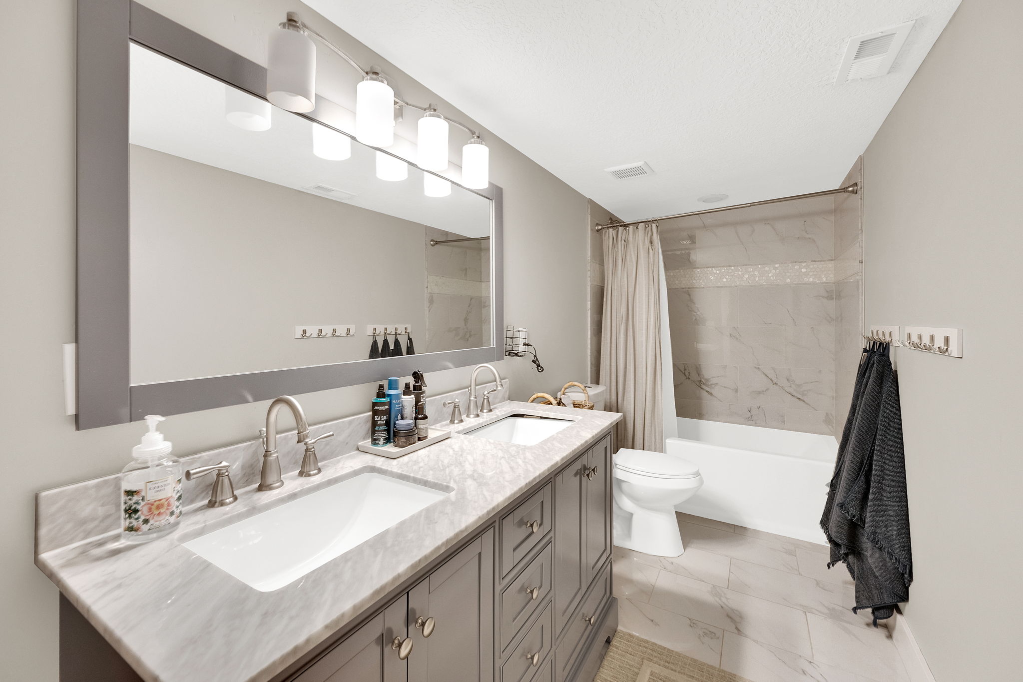 Dual basin vanity with a stone countertop, framed mirror, and contemporary lighting