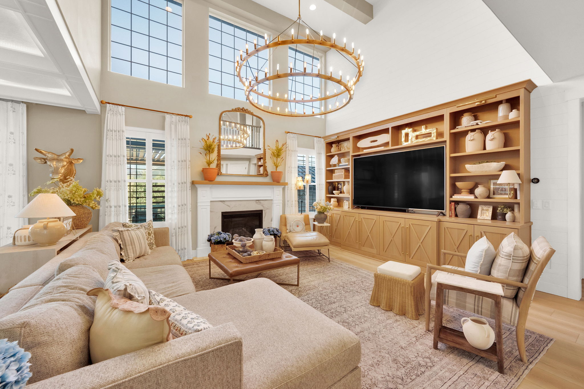 Vaulted ceiling living area featuring a large brass chandelier, a built-in media center with wood-finish cabinetry, a fireplace with a mantel, and tall windows