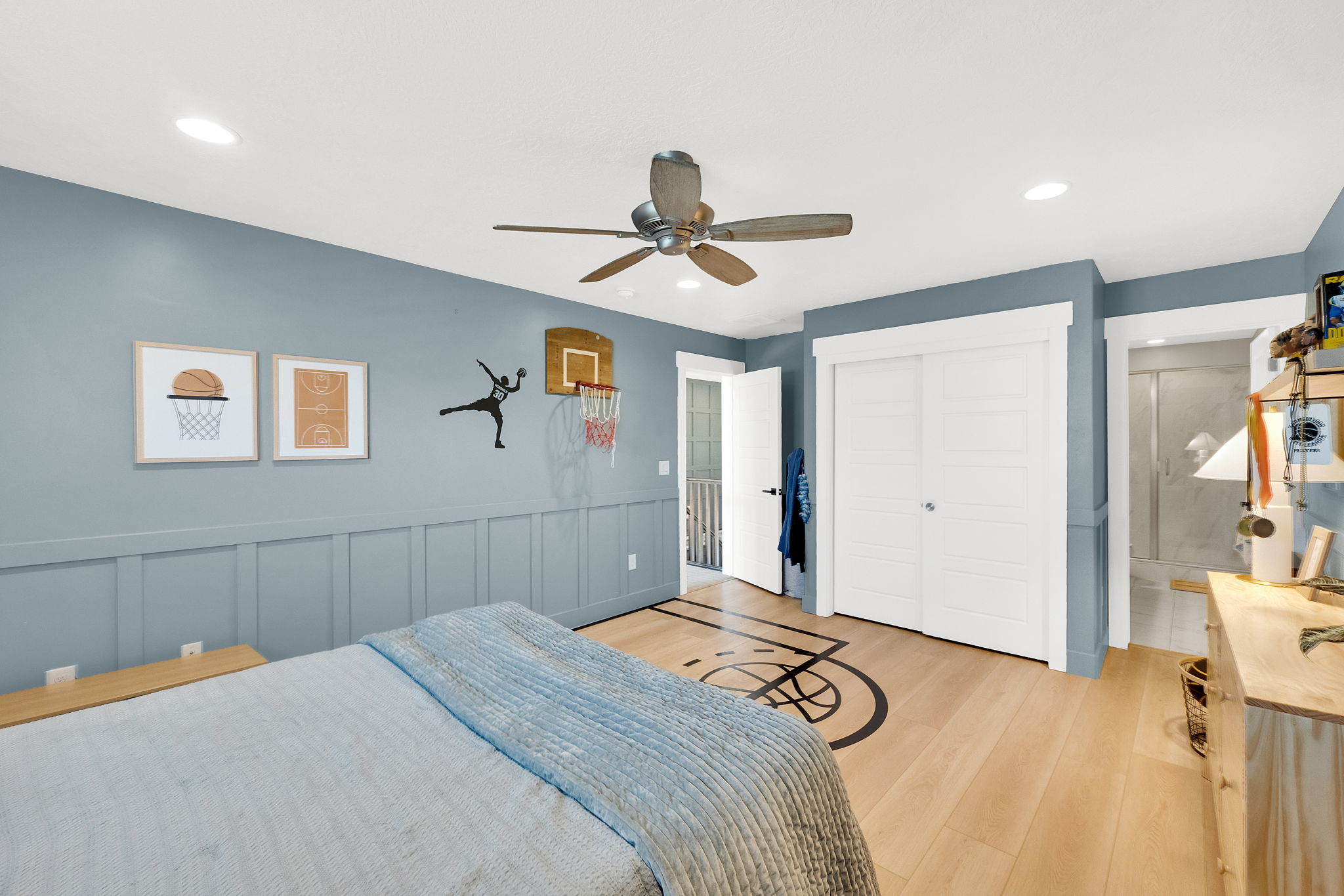 Light wood-finish flooring with an integrated graphic, ceiling fan, recessed lighting, and board and batten wall paneling