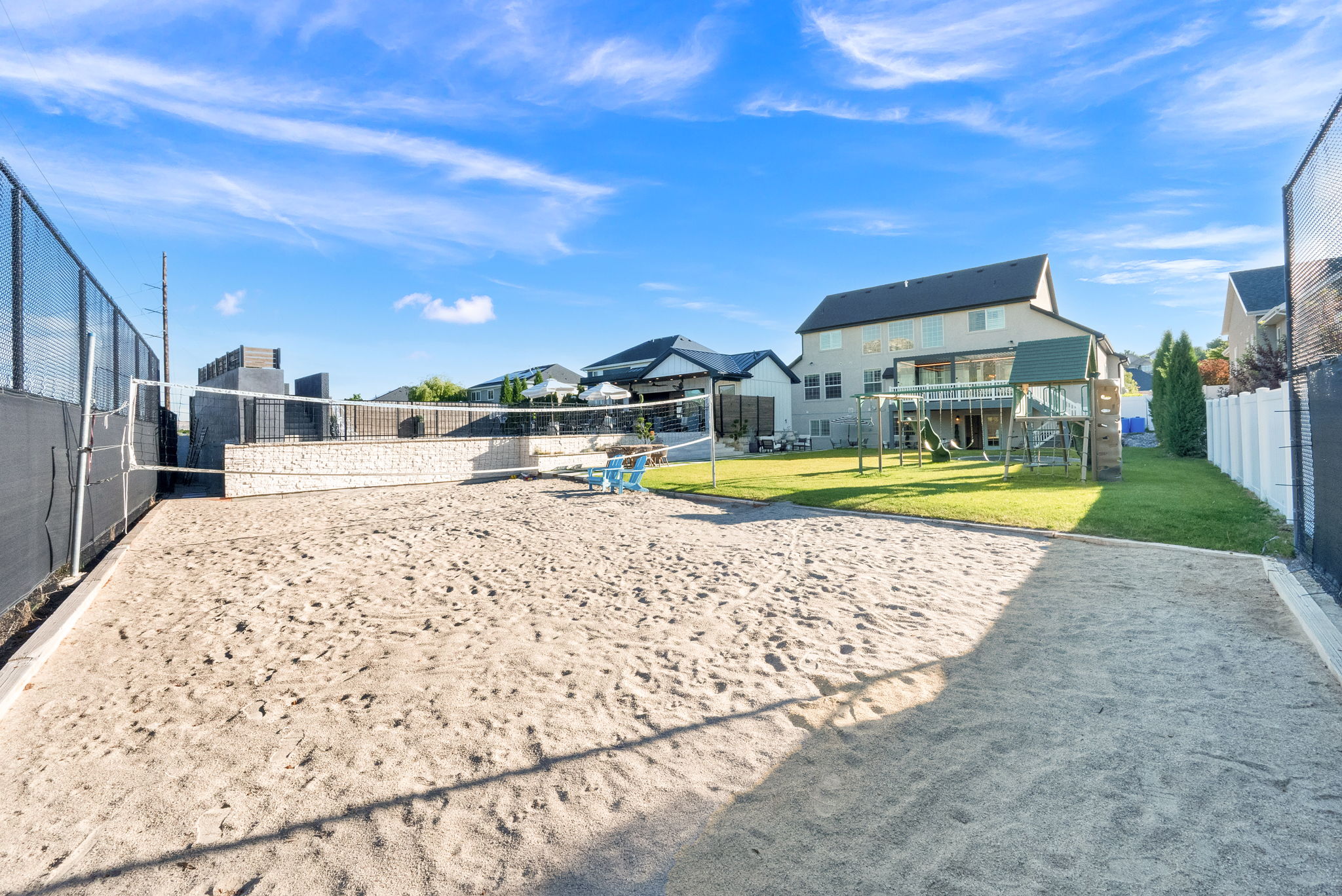 Backyard sand volleyball court with net, framed by a black chain-link fence