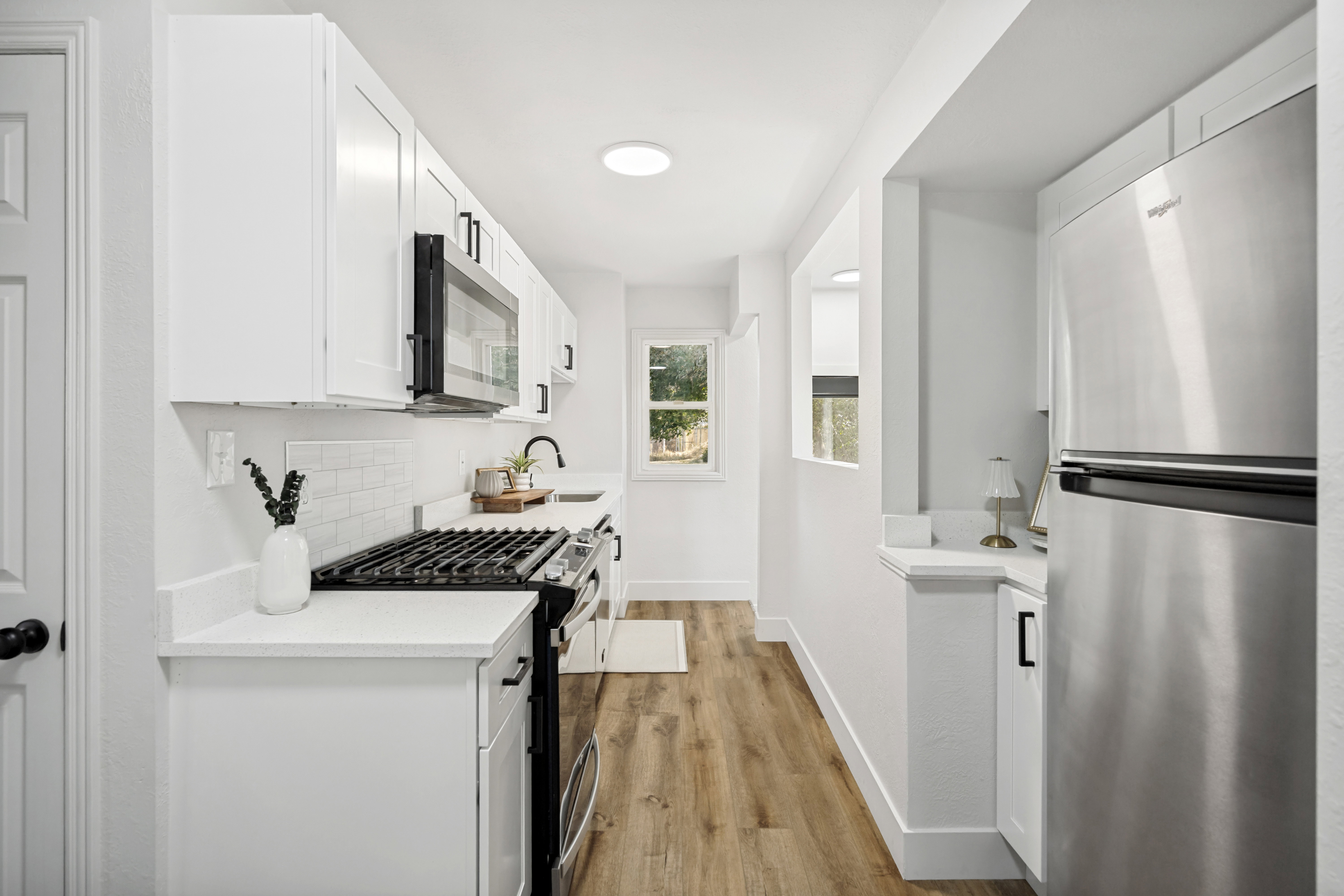 Contemporary kitchen featuring white cabinetry, subway tile backsplash, stone-finish countertops, stainless steel appliances, and wood-finish flooring