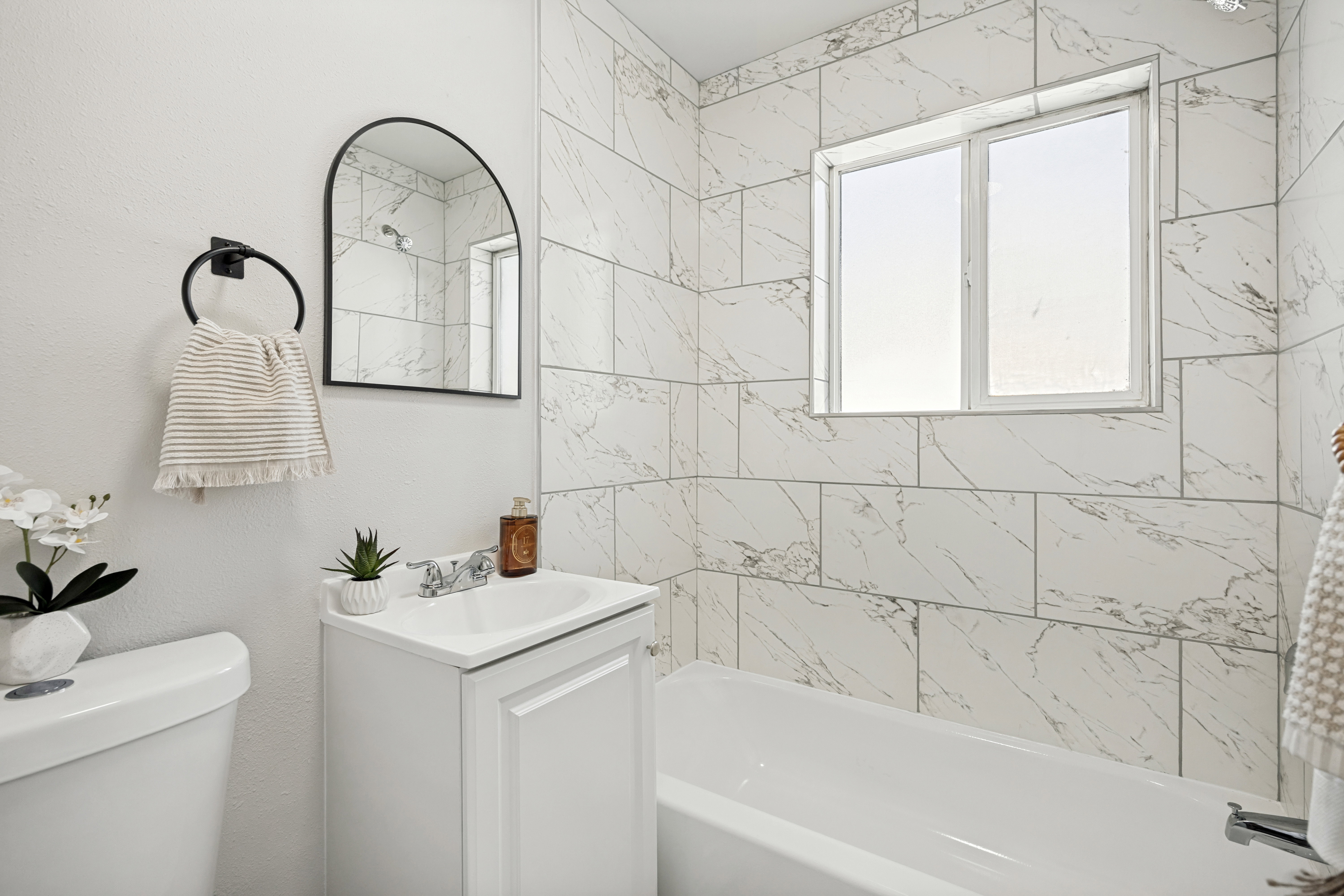 Bathroom featuring a white vanity with a single basin sink, an arched black-framed mirror, and a full bathtub with white subway tile surround