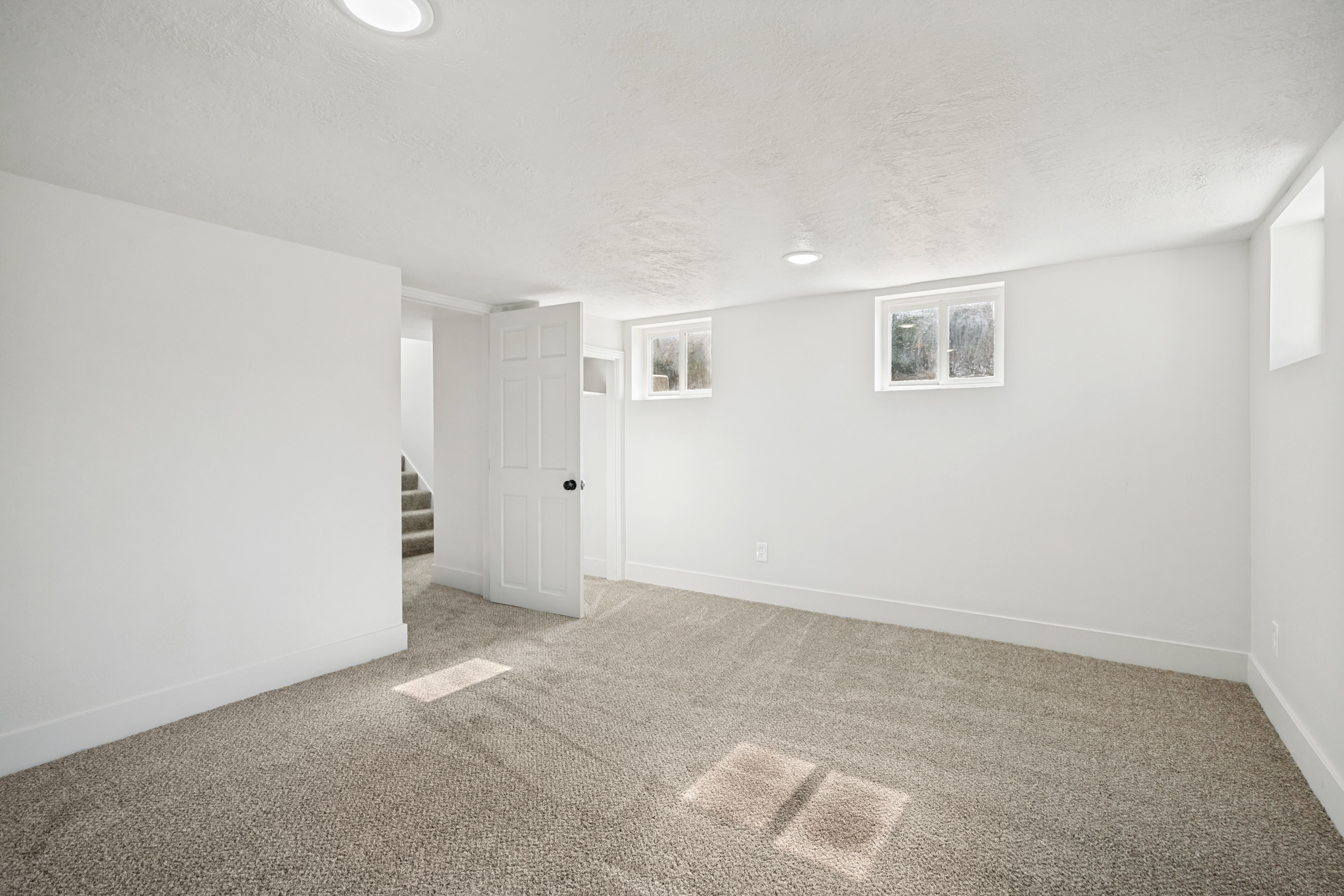 Spacious room featuring neutral carpeting, white walls, recessed lighting, and multiple windows