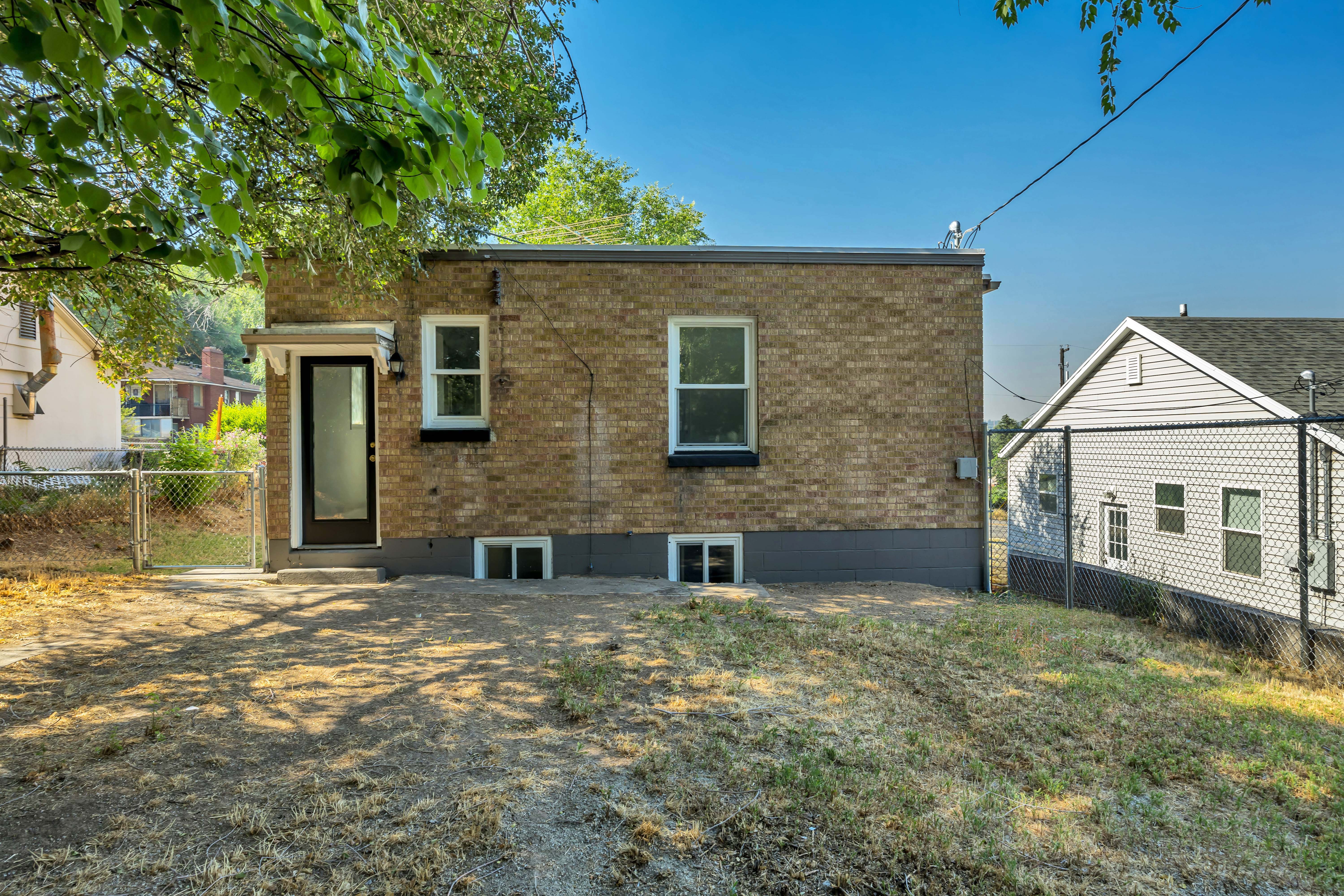 Brick exterior featuring a rear entry door with an awning, multiple windows, and a partially fenced yard