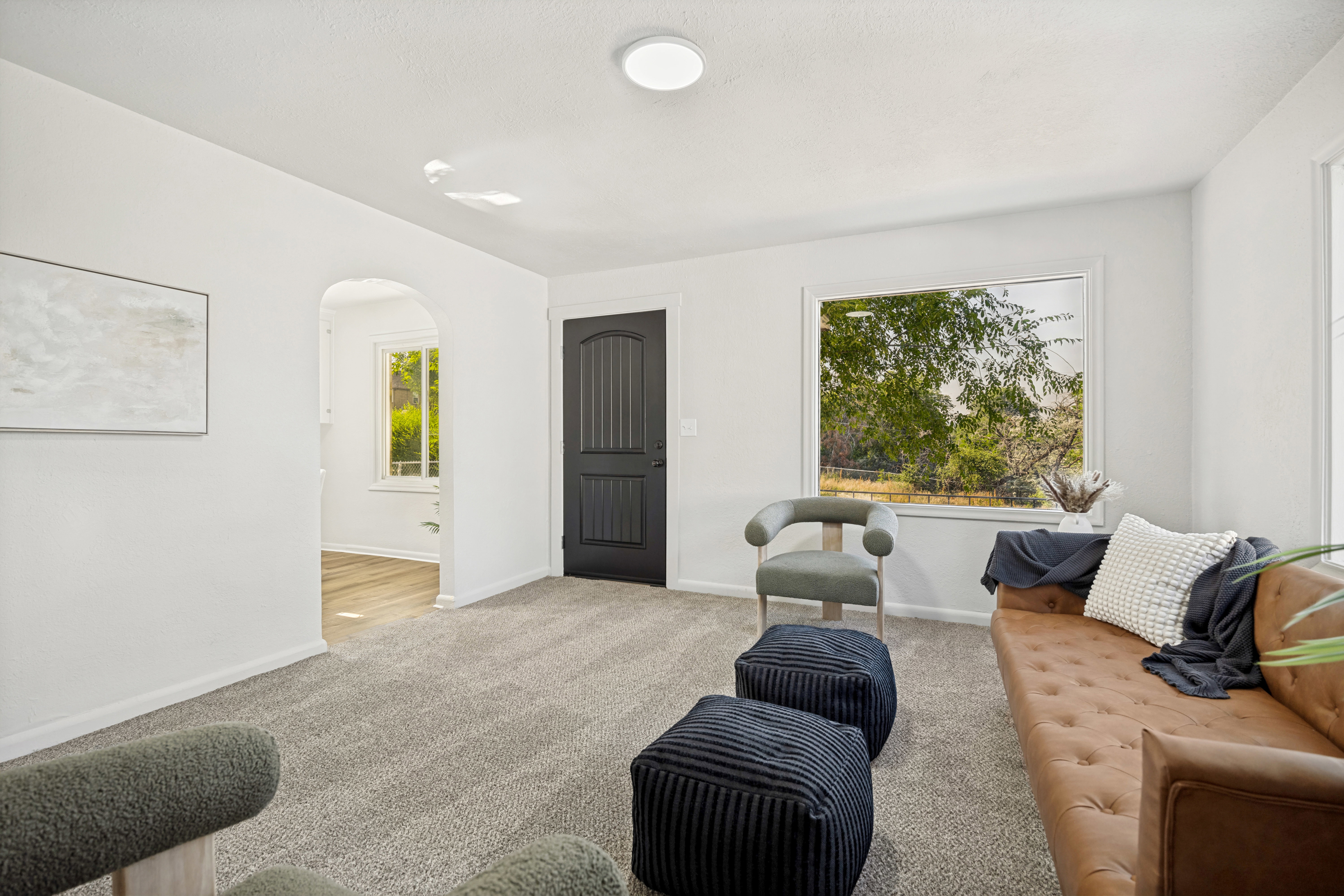Spacious living area featuring light-toned walls, textured carpet, and a large window with outdoor scenery