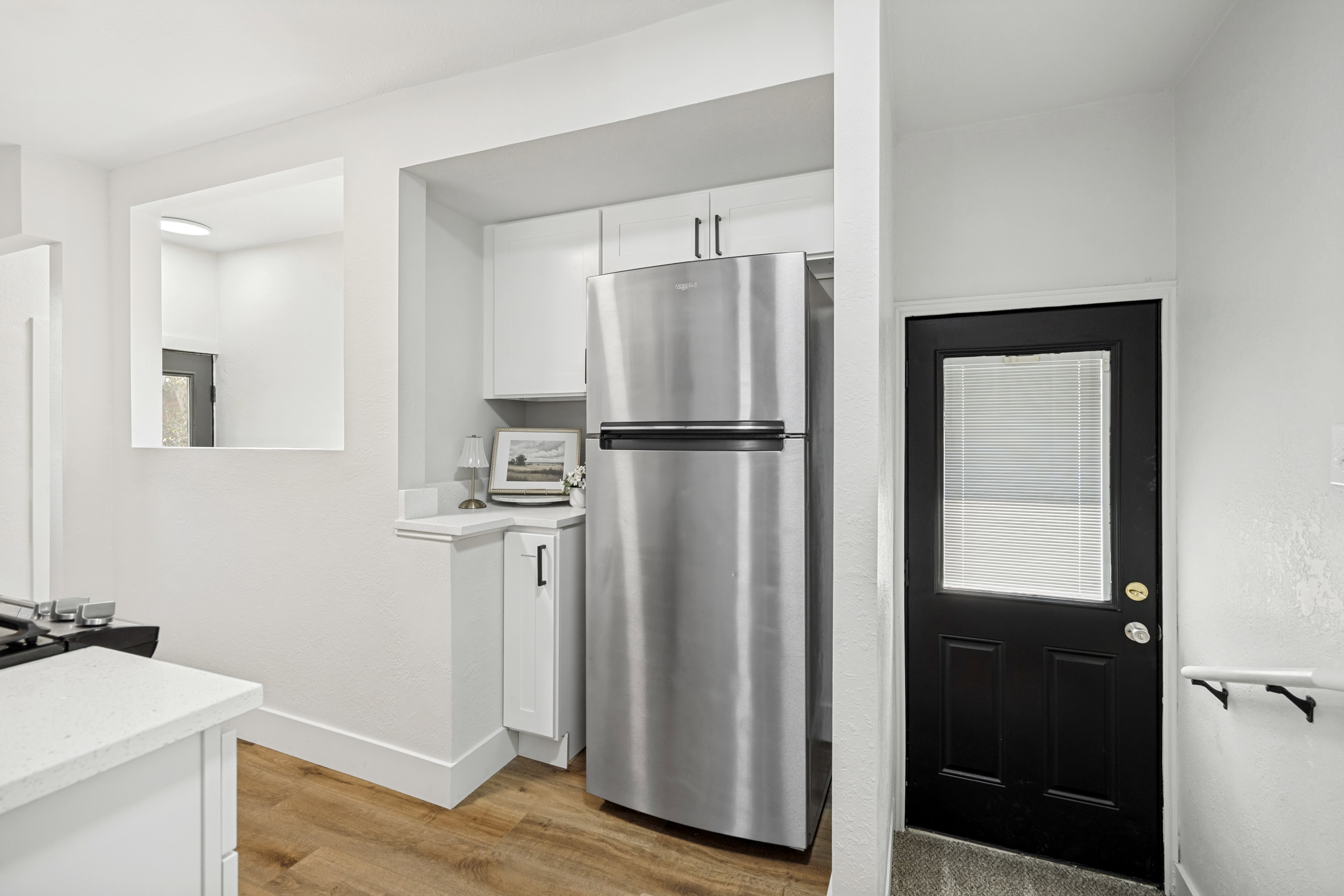 Kitchen area featuring a stainless steel refrigerator, white cabinetry with dark hardware, and wood-finish flooring