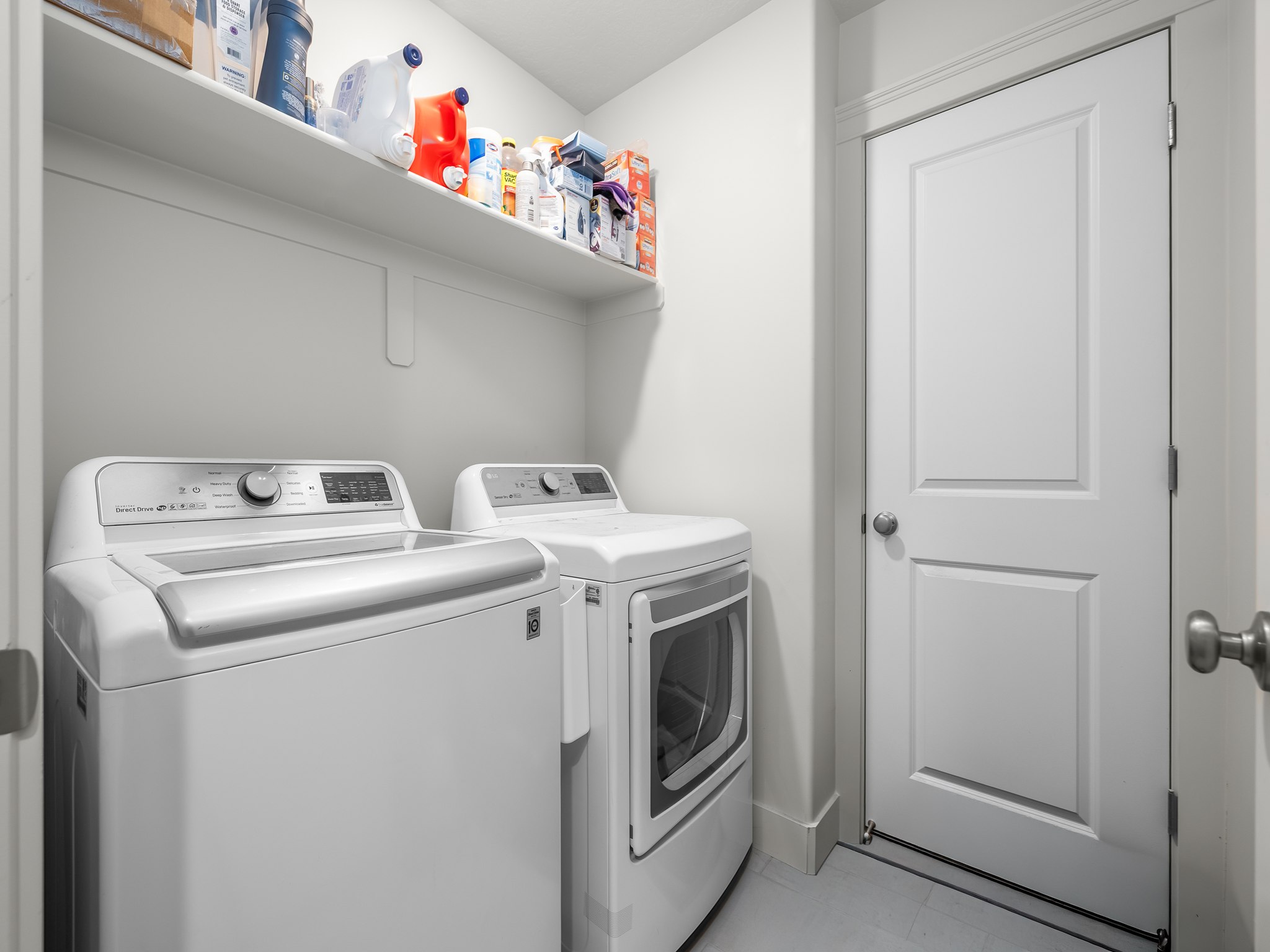 Laundry area featuring a built-in shelf, two permanent appliance hookups, a paneled interior door with a round knob, and light-toned flooring