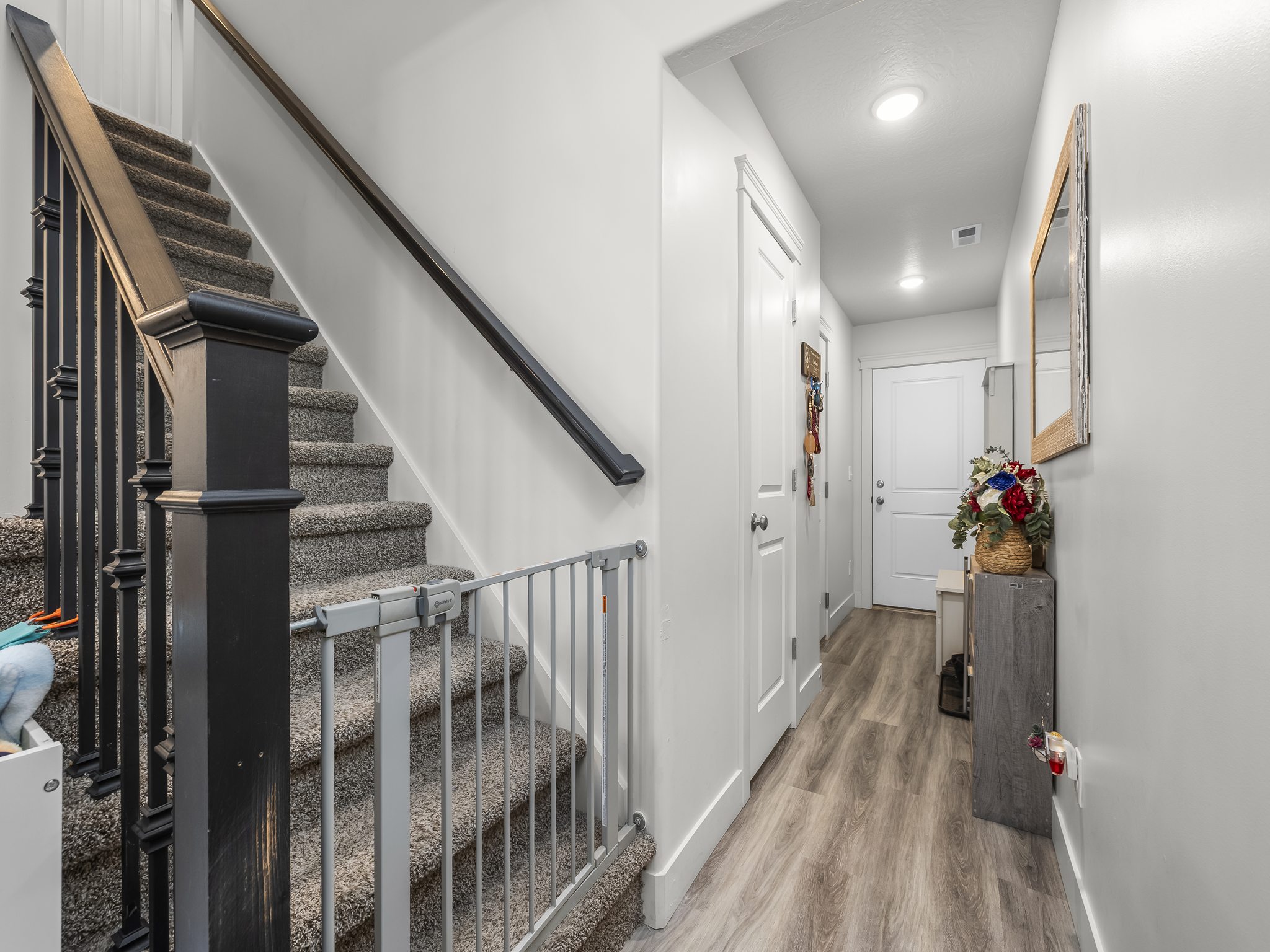 Carpeted staircase with dark wood newel post and balusters, featuring a light wood-finish flooring hallway with white walls, recessed lighting, and white paneled doors