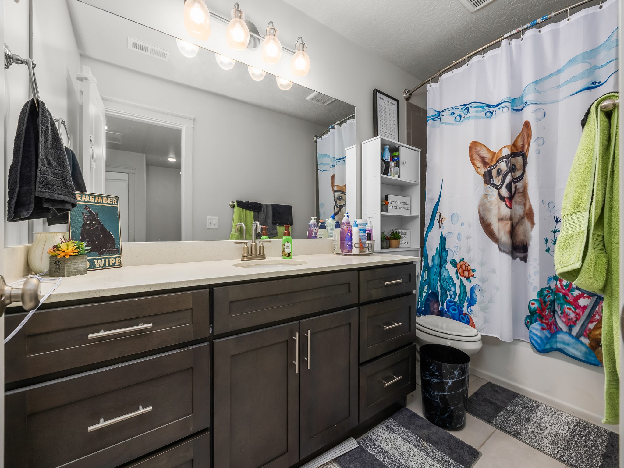 Bathroom featuring a dark wood-finish vanity with a light-toned countertop, a large wall-mounted mirror, and a built-in shower/tub combination