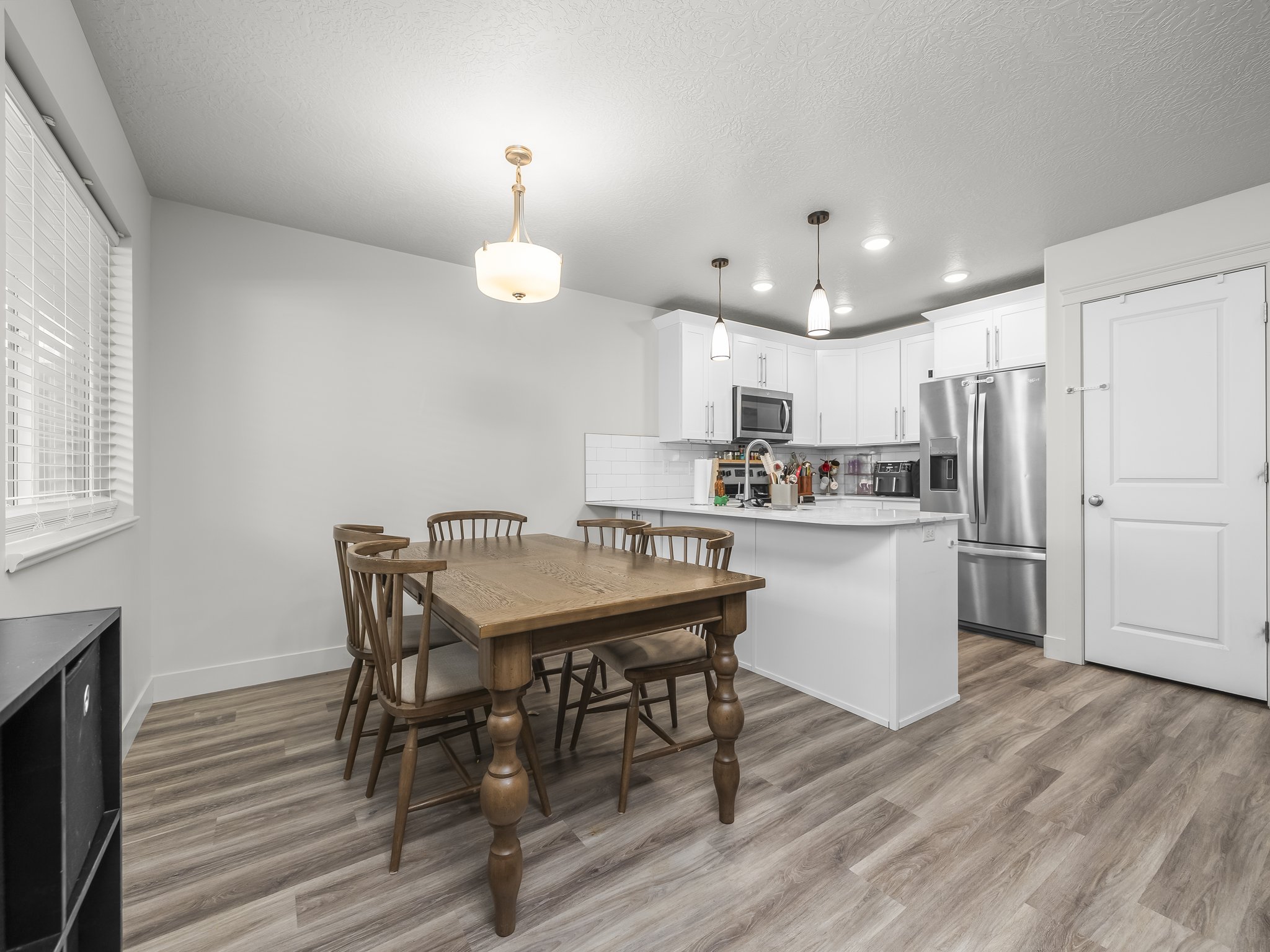 Open-concept kitchen and dining area featuring light wood-finish flooring, white cabinetry, stainless steel appliances, and a tile backsplash