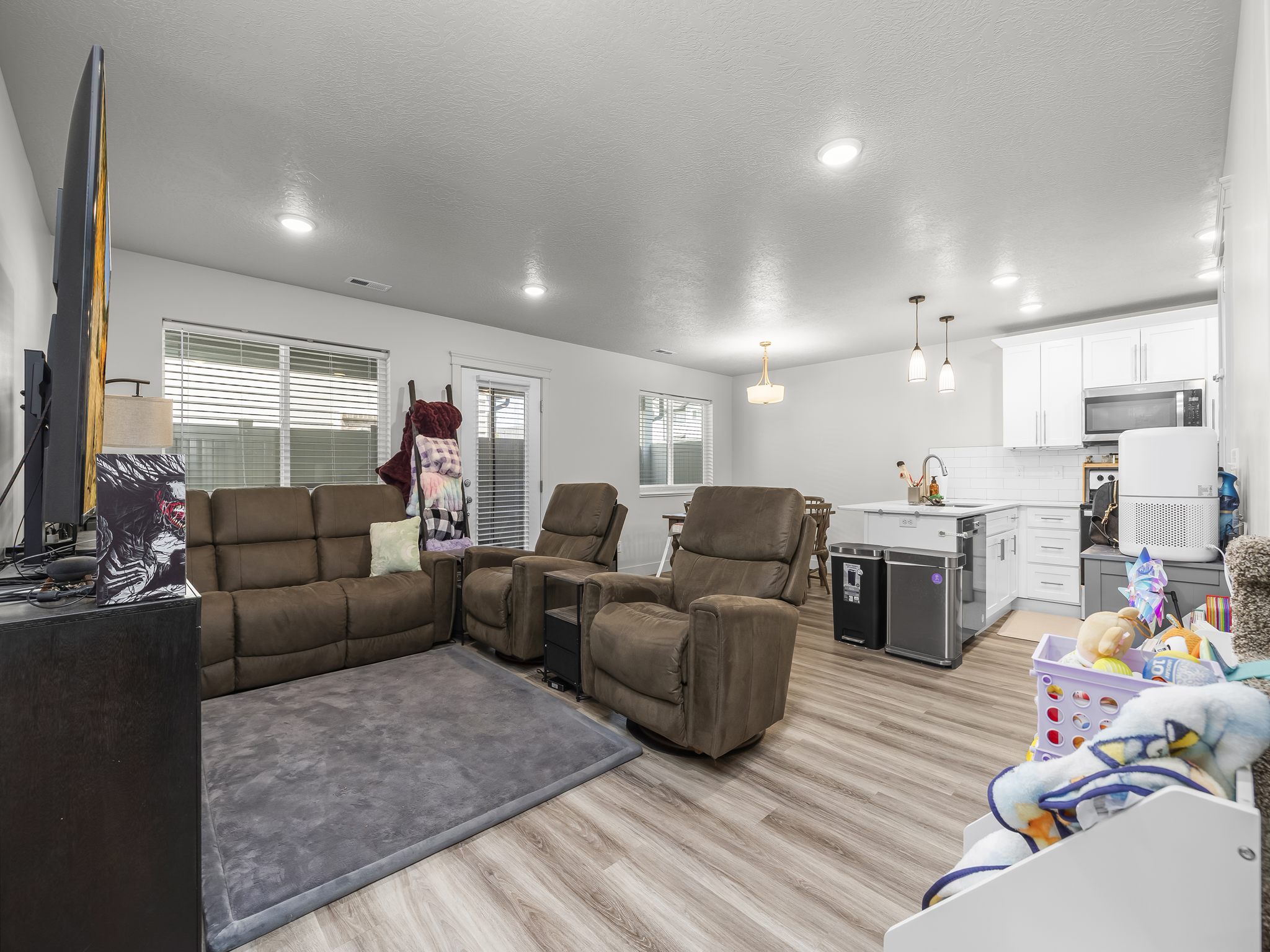 Open-concept living space featuring wood-finish flooring throughout, white walls, and recessed lighting