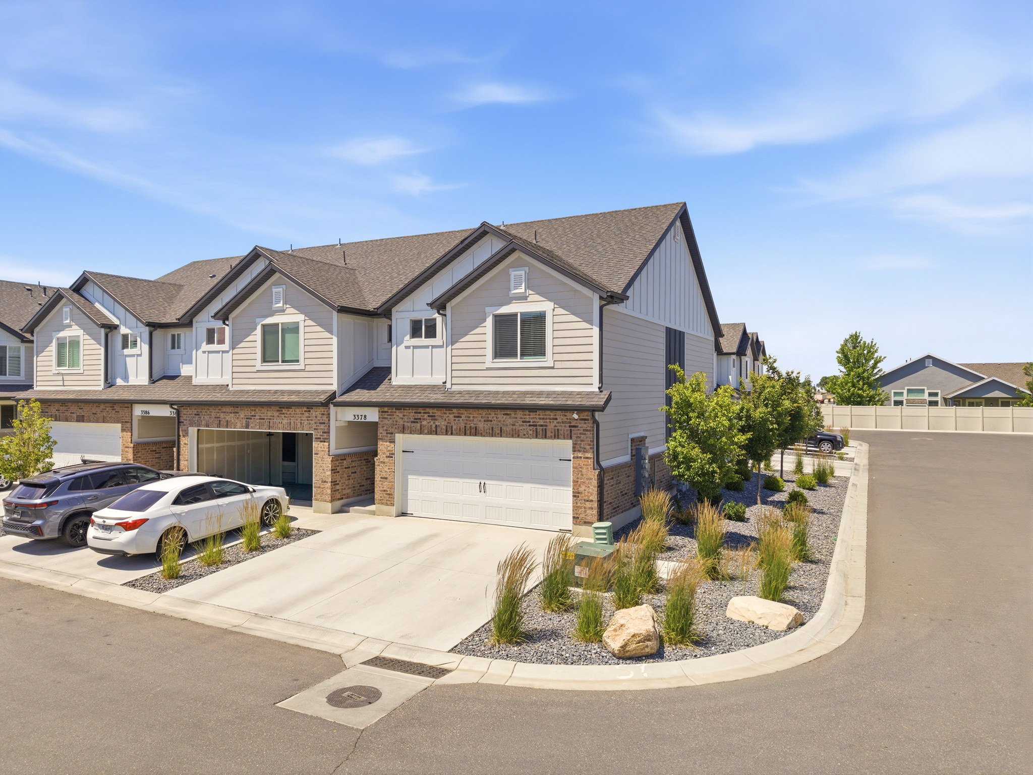 Contemporary townhome exterior featuring light-toned siding, dark shingle roofing, and brick accents