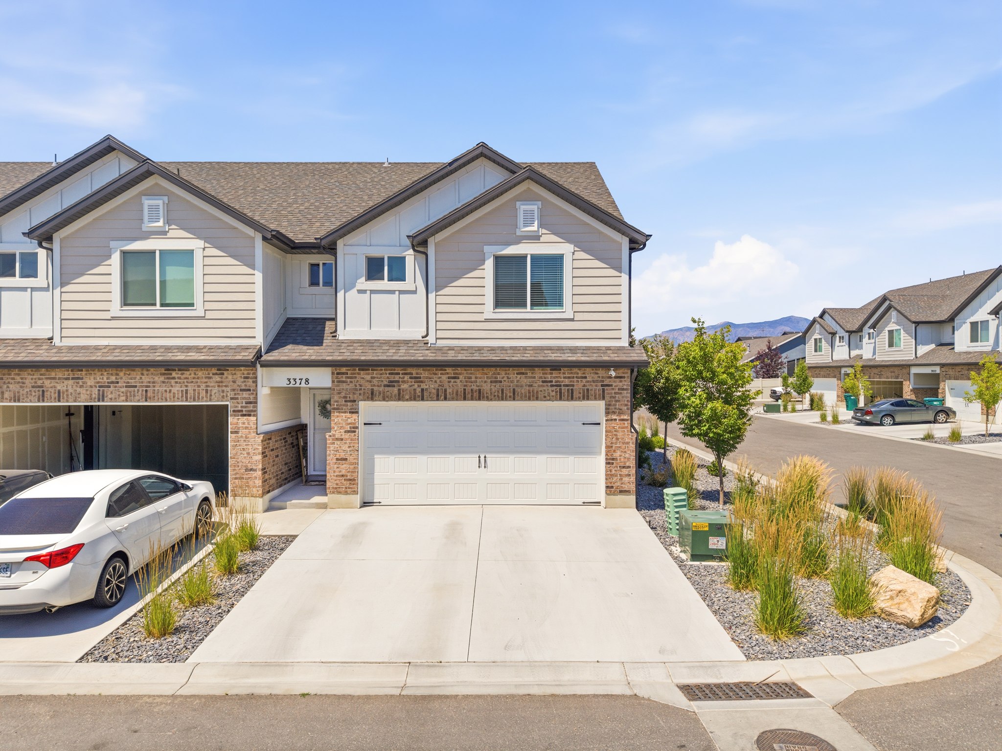 Contemporary townhome featuring a two-car garage, brick facade, light-toned siding, and a concrete driveway