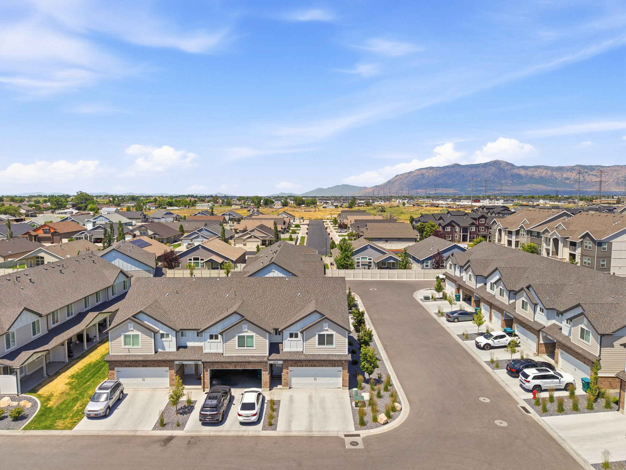 Modern townhome community featuring a paved street, attached garages, landscaping, and a mountainous backdrop