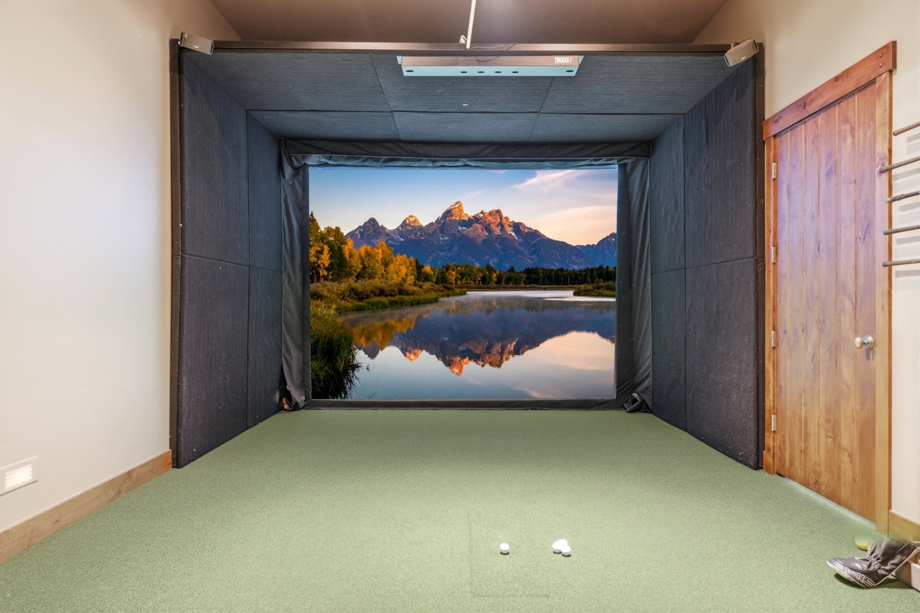Dedicated golf simulator room featuring a large projection screen, light green turf flooring, recessed lighting, a wooden door, and light wood baseboards