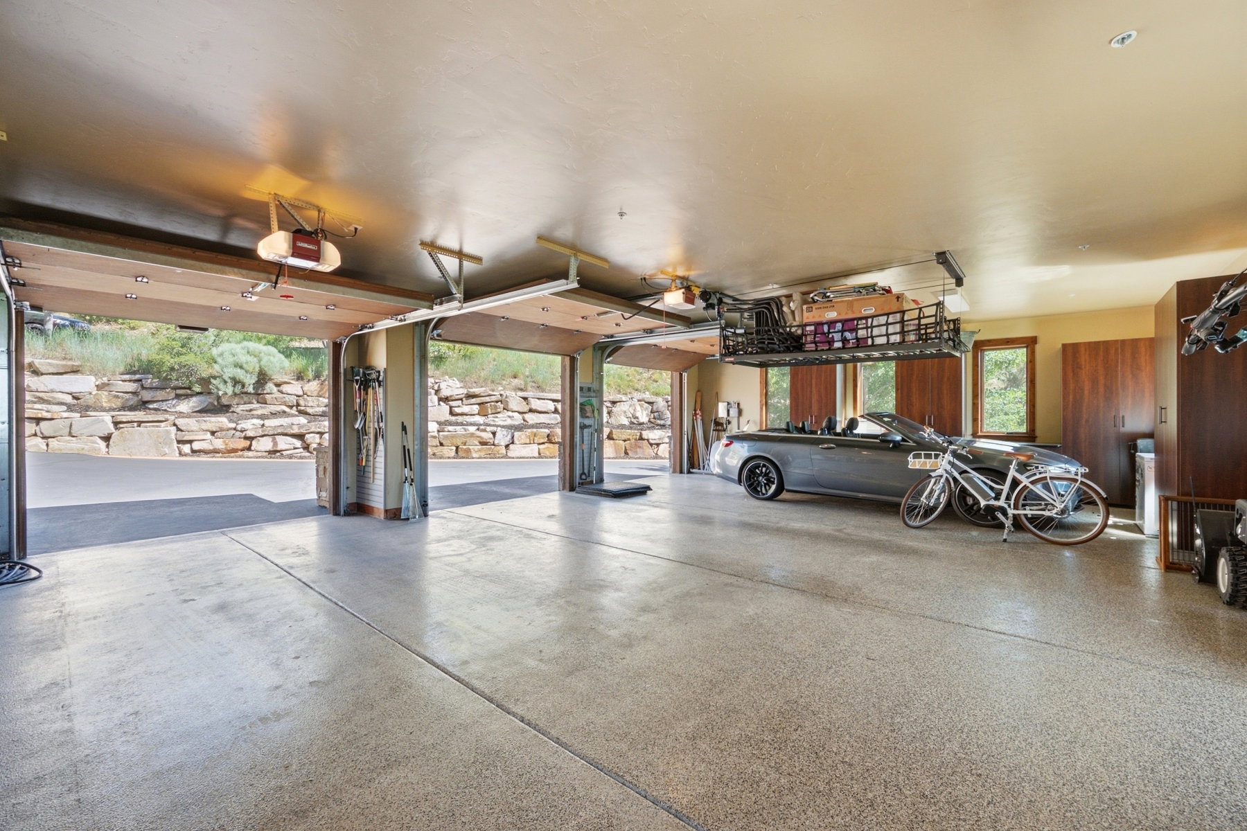 Multi-car garage featuring two open bay doors, speckled epoxy flooring, built-in cabinetry, and integrated overhead storage
