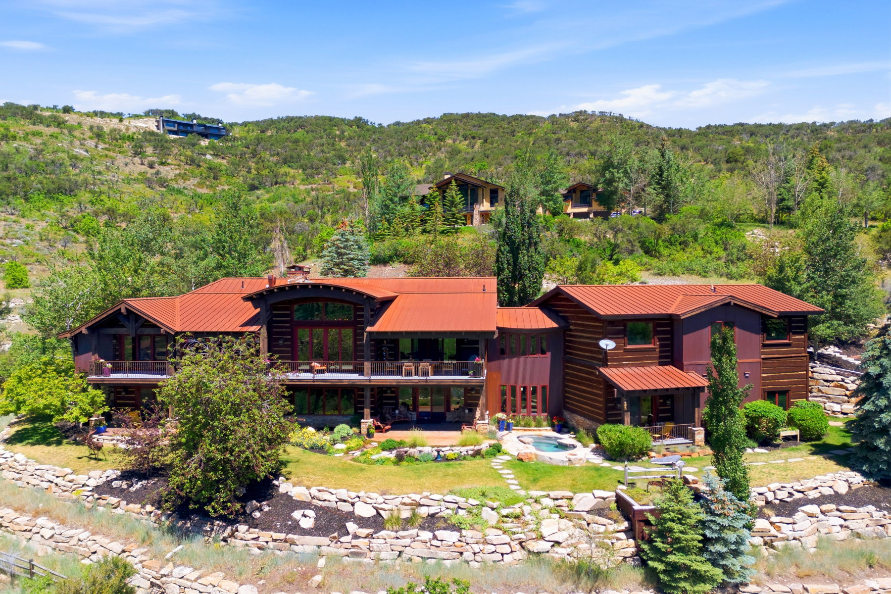 Multi-level log cabin-style residence featuring a prominent red metal roof, multiple balconies, and extensive terraced landscaping