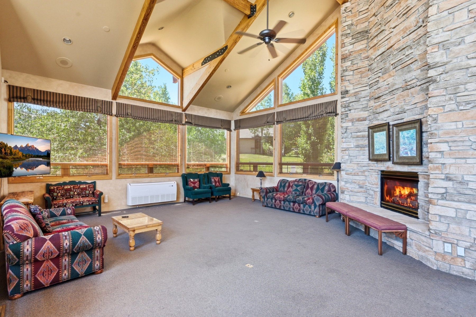 Spacious room featuring a floor-to-ceiling stone fireplace, vaulted ceiling with exposed wood beams, and a ceiling fan