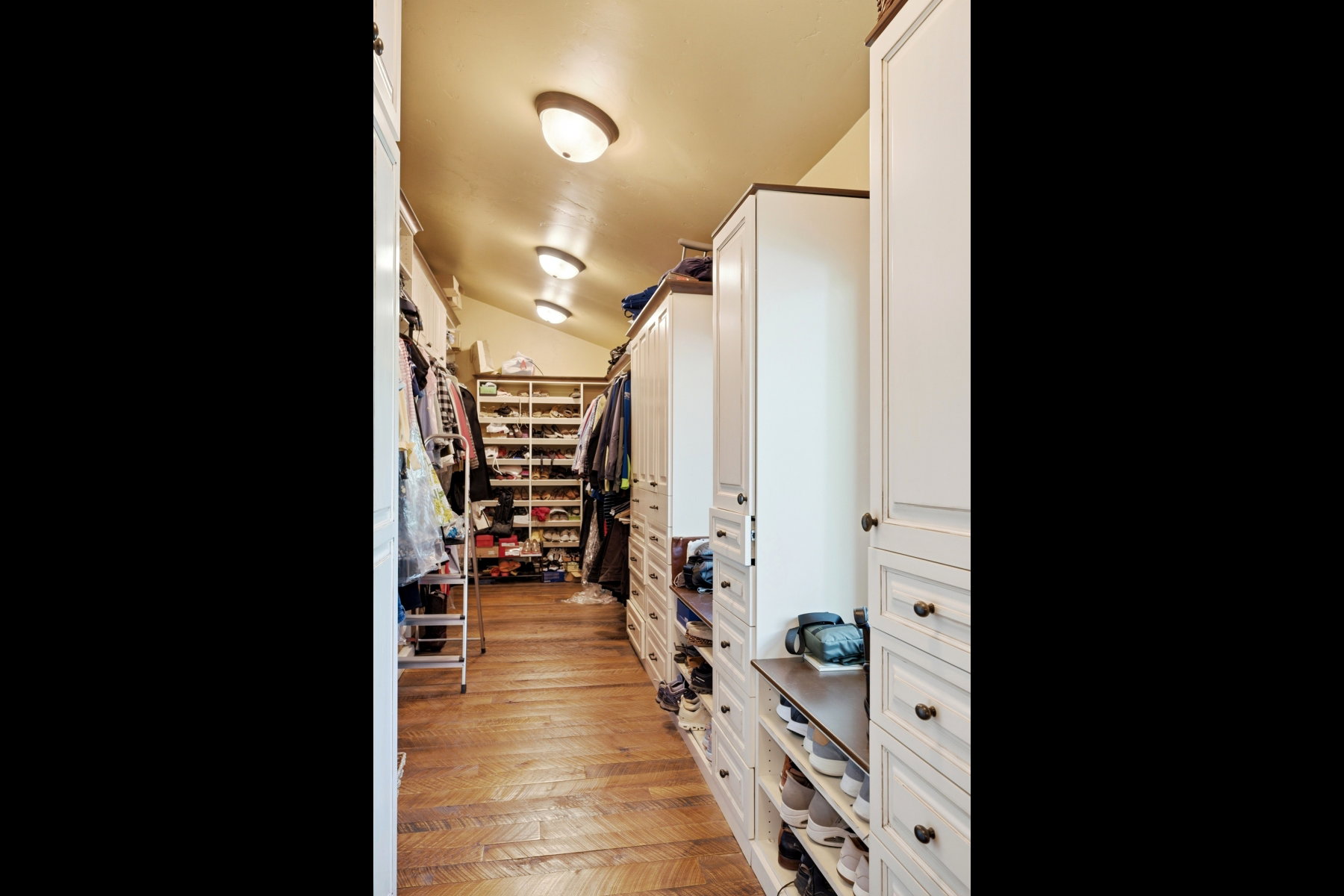 Custom closet system featuring wood-finish flooring, recessed lighting, built-in shelving, drawers, and cabinet storage