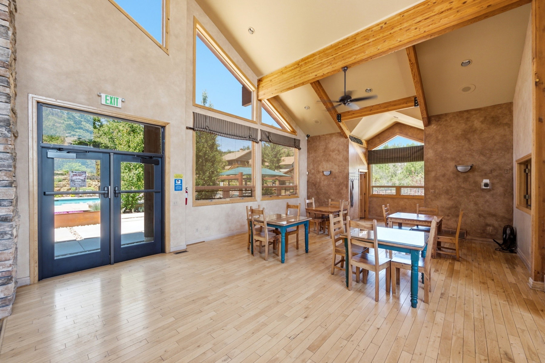 Spacious common area featuring vaulted ceilings with exposed wood beams, light wood-finish flooring, and large windows