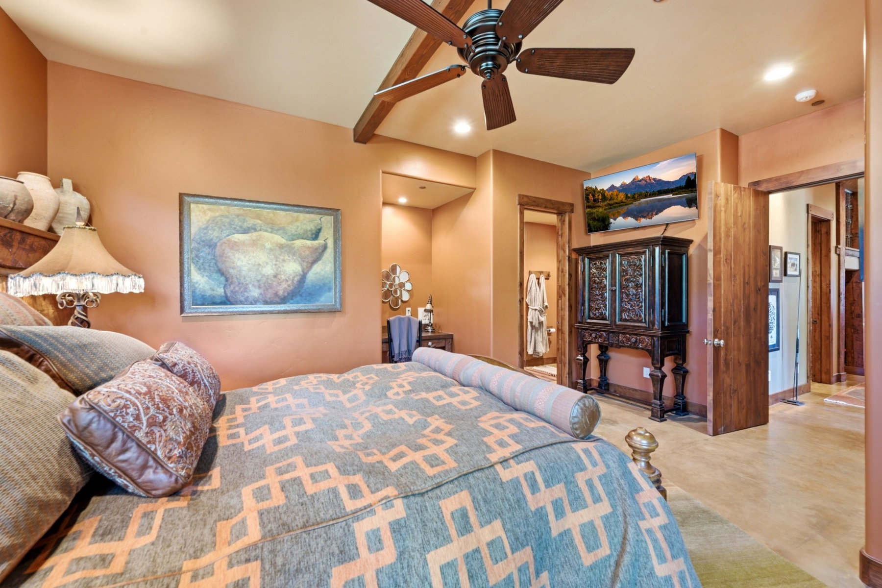 Spacious bedroom featuring warm-toned walls, wood-finish ceiling beams, and a ceiling fan