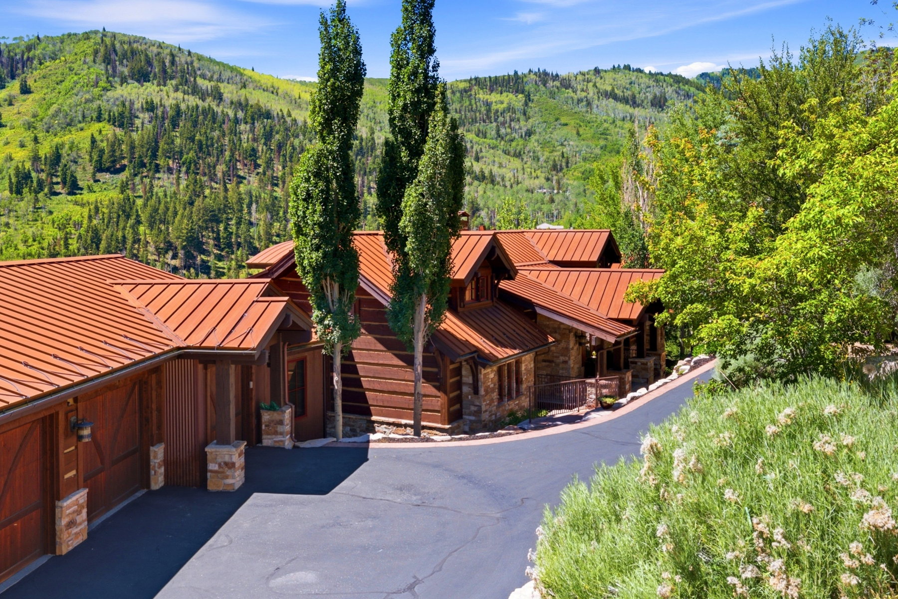 Expansive mountain lodge with a metal roof, stone accents, wood siding, and mature trees