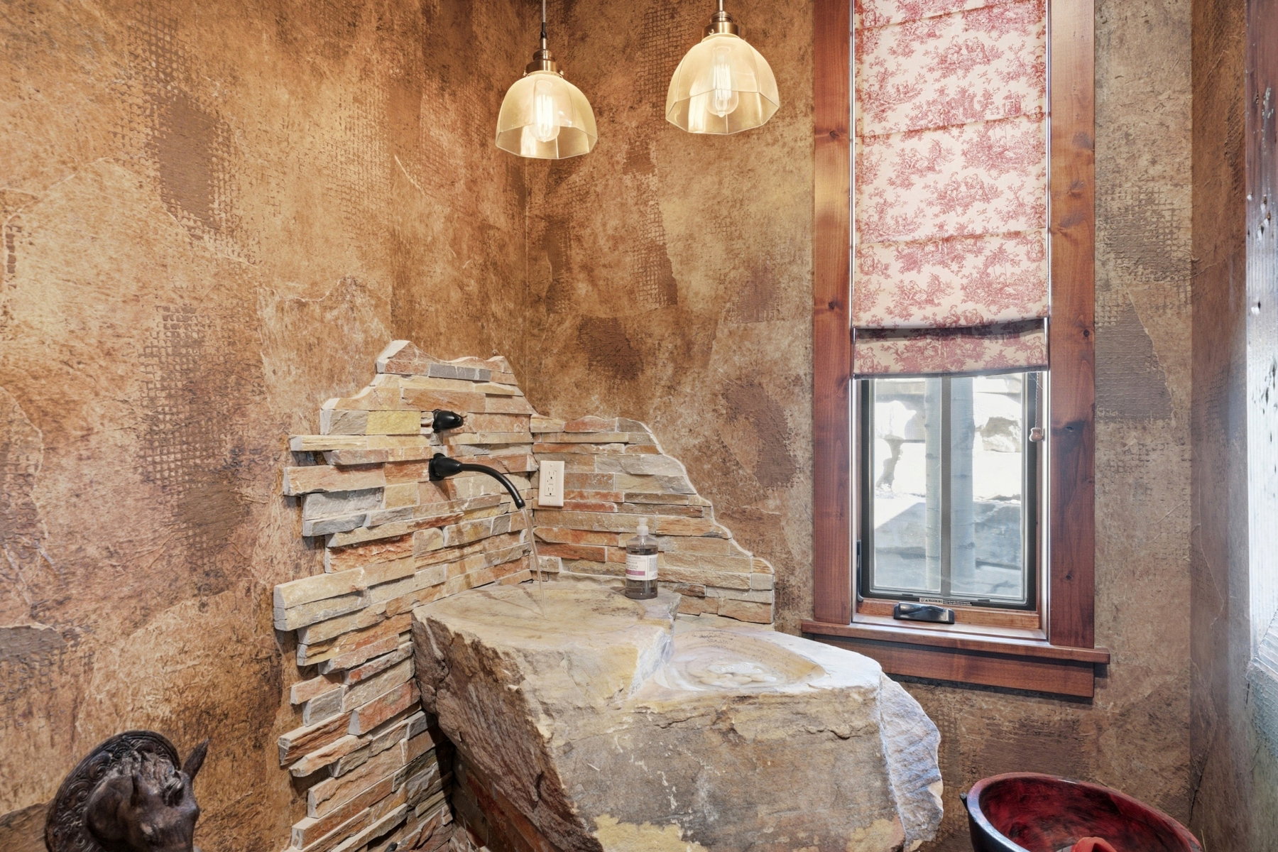 Unique stone sink basin with stacked stone surround, wall-mounted faucet, and two glass pendant lights