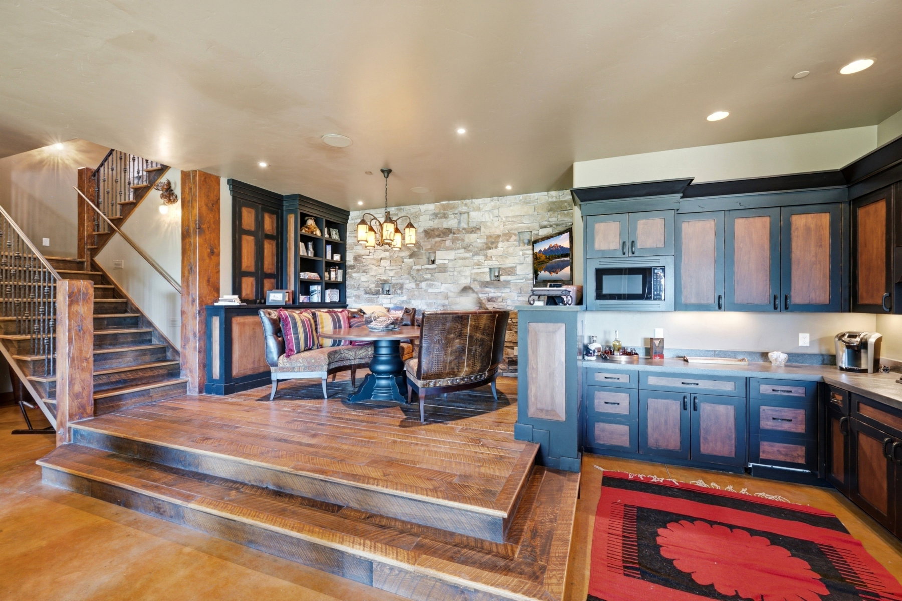 Multi-level interior featuring wood-finish flooring, a stacked stone accent wall, custom built-in cabinetry, an integrated microwave, and an ornate chandelier