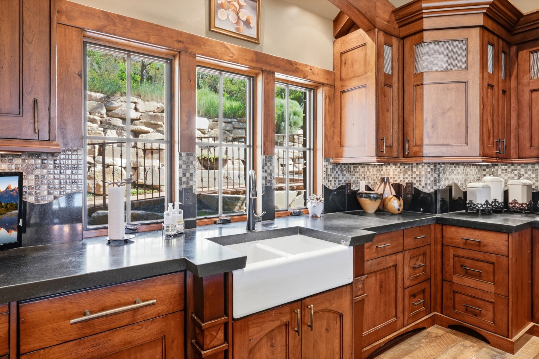 Kitchen featuring extensive wood cabinetry, dark countertops, a white farmhouse-style sink, and mosaic tile backsplash