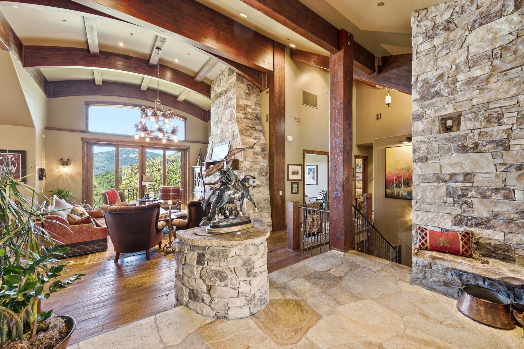 Expansive interior featuring high vaulted ceilings with exposed wood beams, a stone accent wall, wood-finish flooring, and large glass doors opening to the exterior