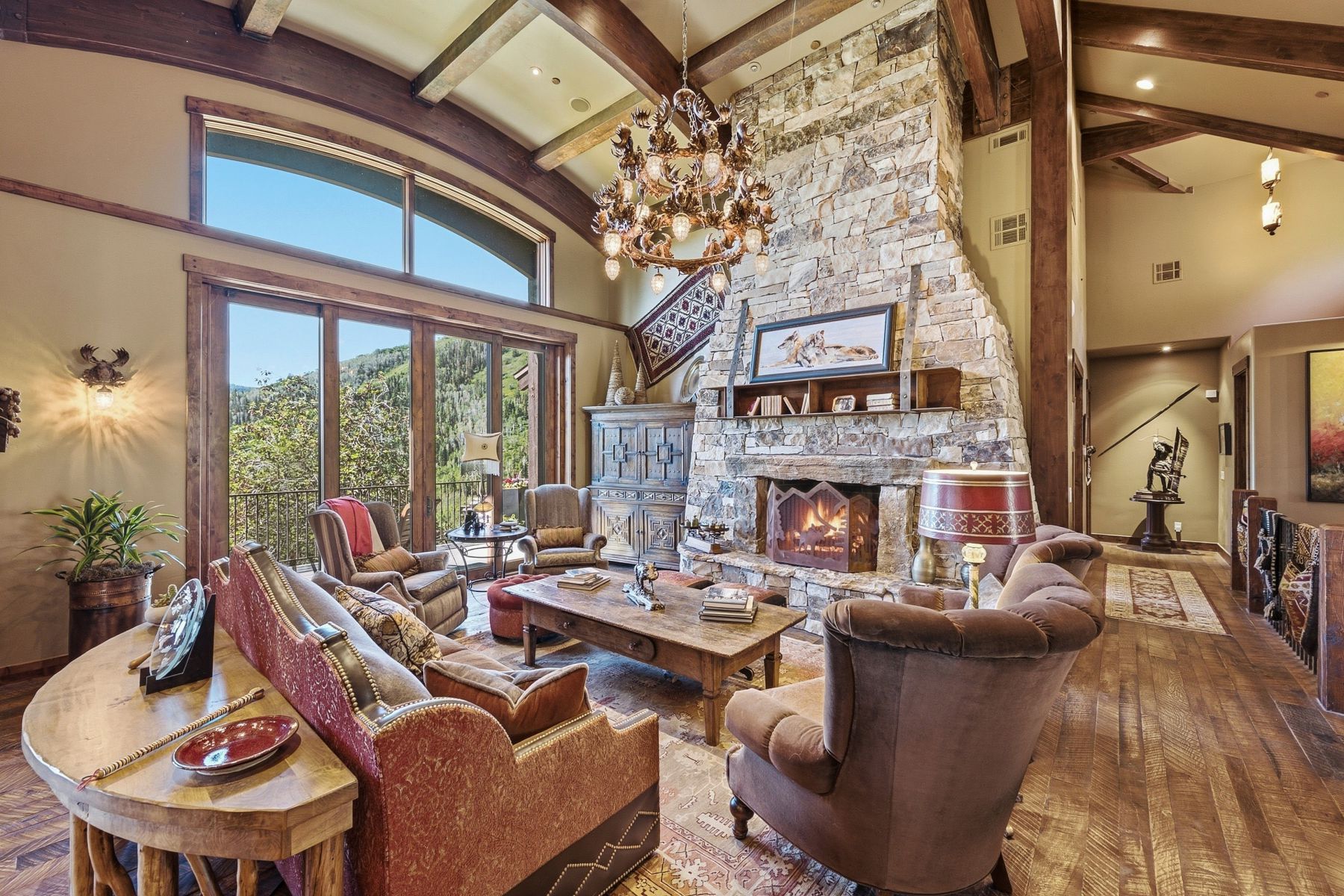 Great room featuring a vaulted ceiling with exposed wood beams, a stone fireplace with a substantial hearth, and expansive windows offering mountain scenery