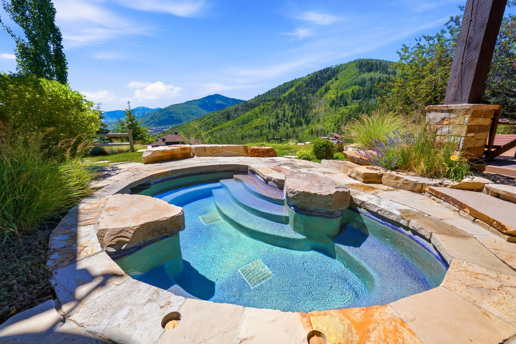 Custom-designed spa featuring integrated stone steps and a surrounding natural stone patio