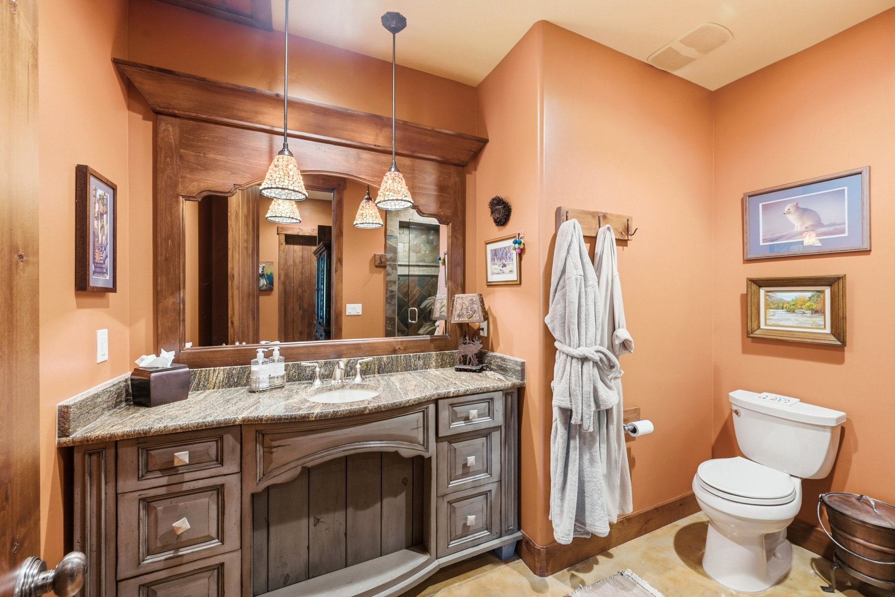 Bathroom featuring an expansive wood-framed mirror, dual pendant lighting, a built-in vanity with a granite-style countertop, and a white toilet