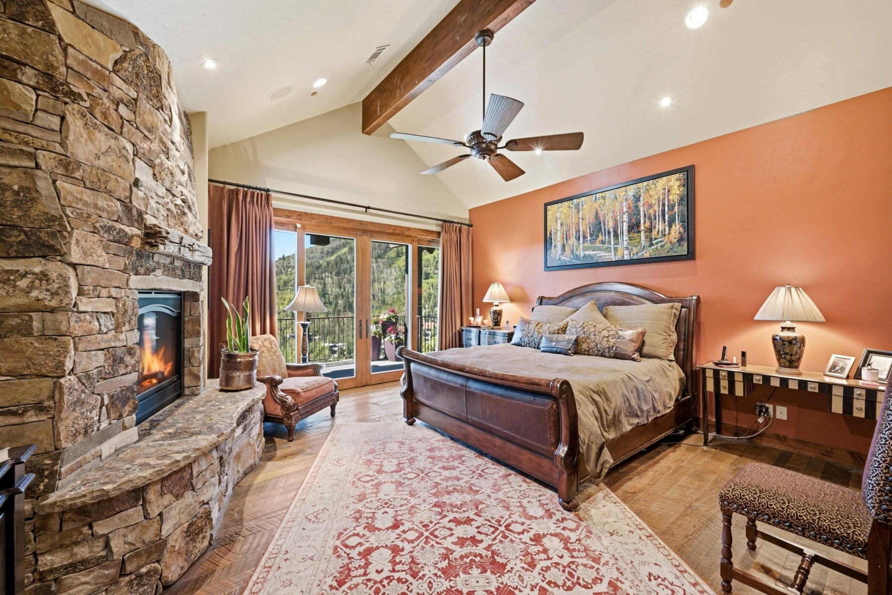 Spacious room featuring a stone fireplace, wood-finish flooring, vaulted ceiling with exposed beam, and direct access to an exterior balcony