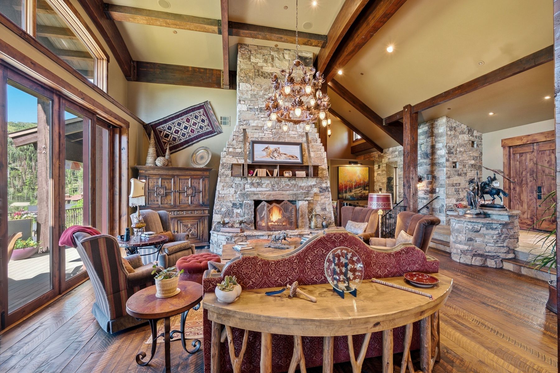 Spacious living area featuring a vaulted ceiling with exposed wood beams, a prominent stone fireplace, and wide plank wood-finish flooring
