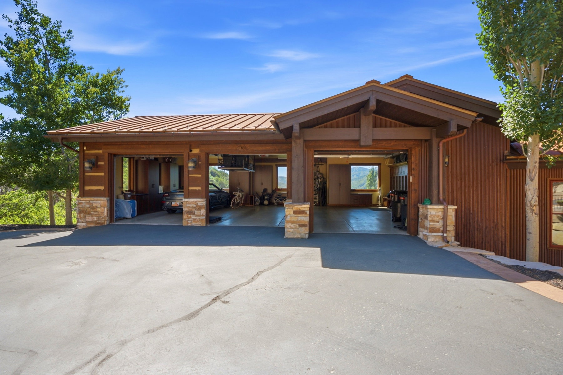 Three-bay garage with exposed wood beams, stone pillar accents, and a metal roof