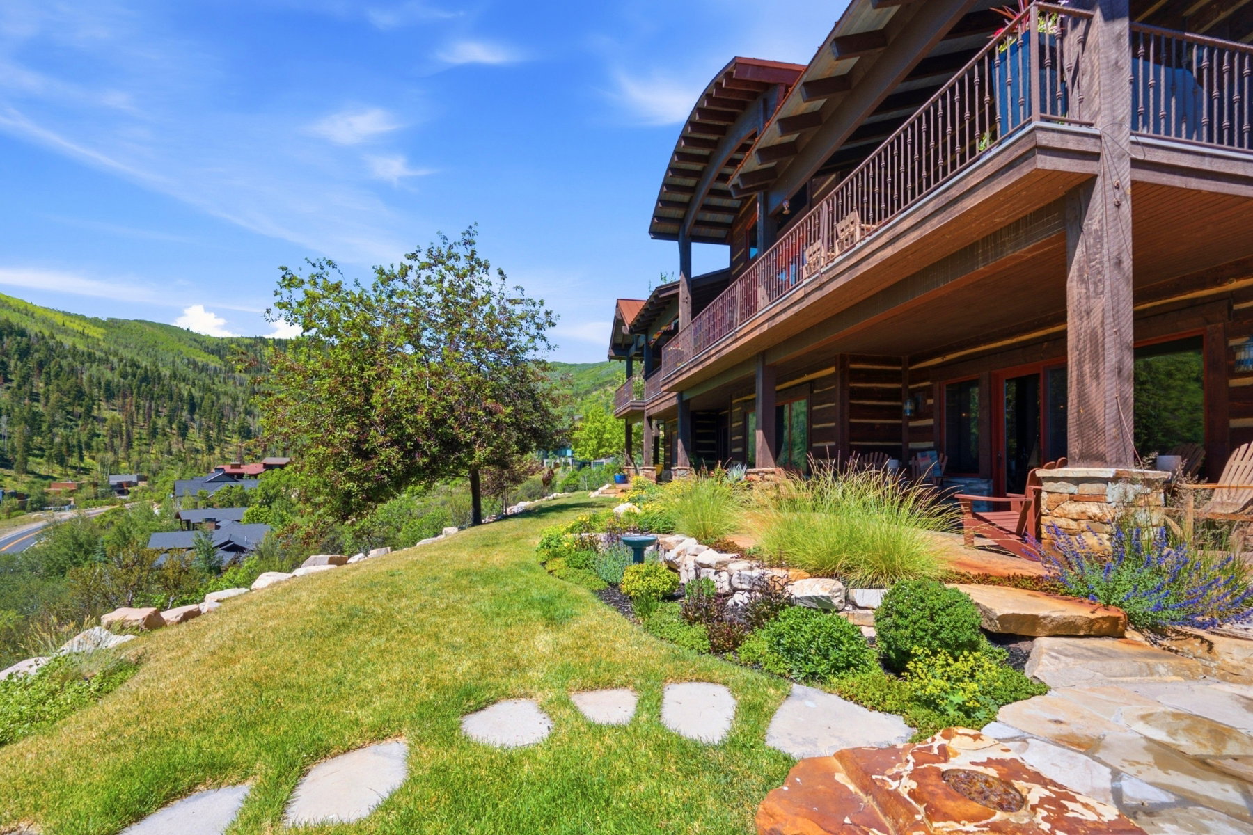 Multi-level log cabin-style exterior featuring a curved upper balcony with wood railings and stone pillars