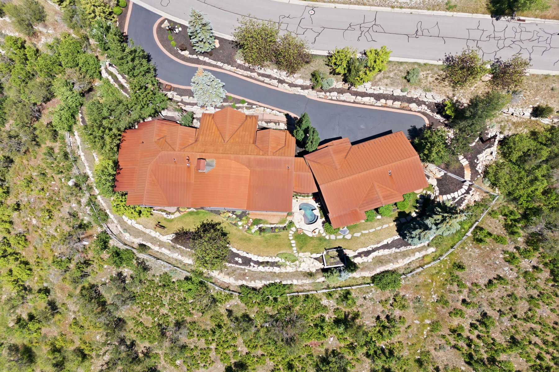 Terracotta-tiled roof property featuring a private driveway, terraced landscaping with stone retaining walls, a built-in swimming pool, and surrounding natural foliage