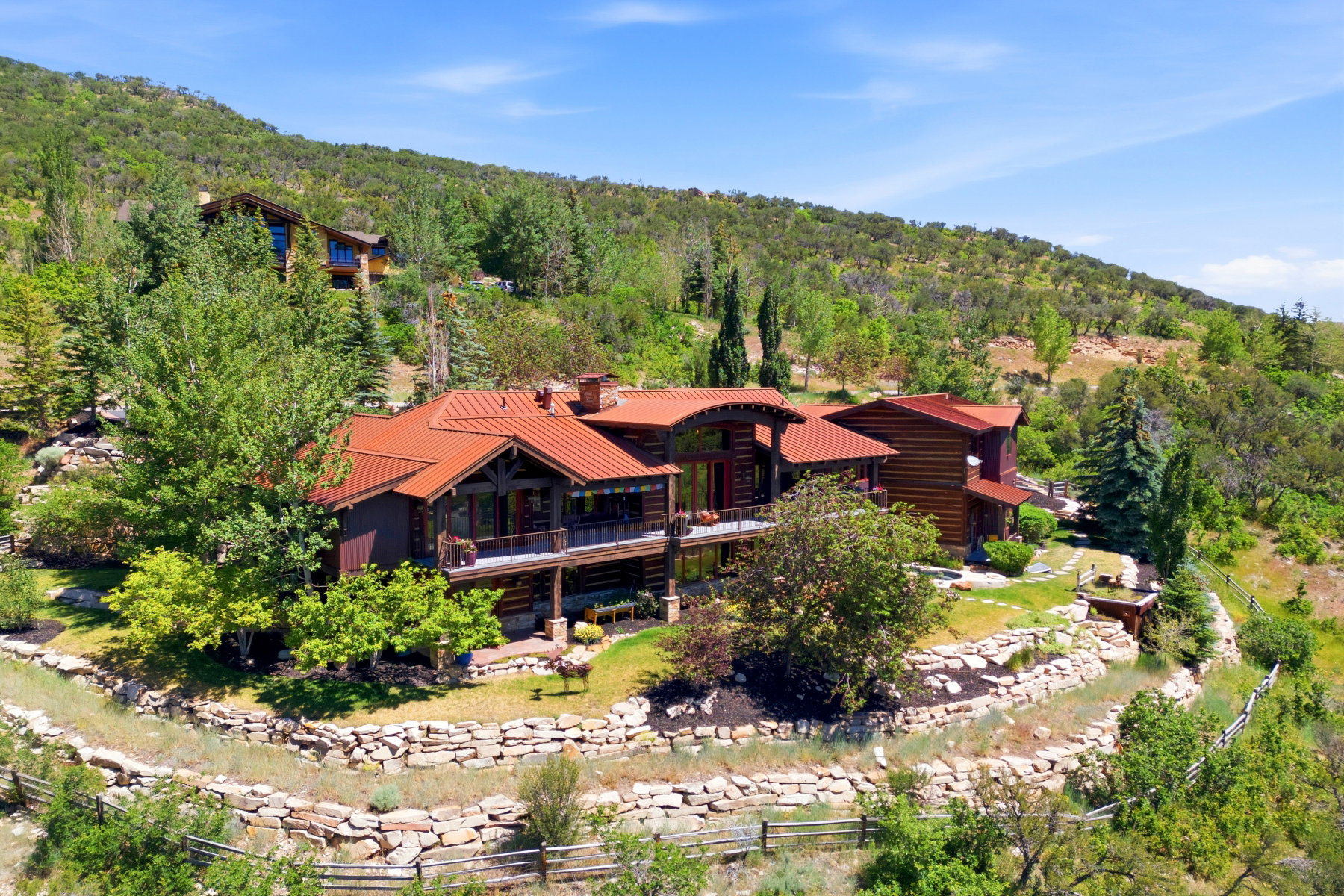 Multi-level residence featuring a rust-toned metal roof, exposed timber beams, and a wrap-around balcony