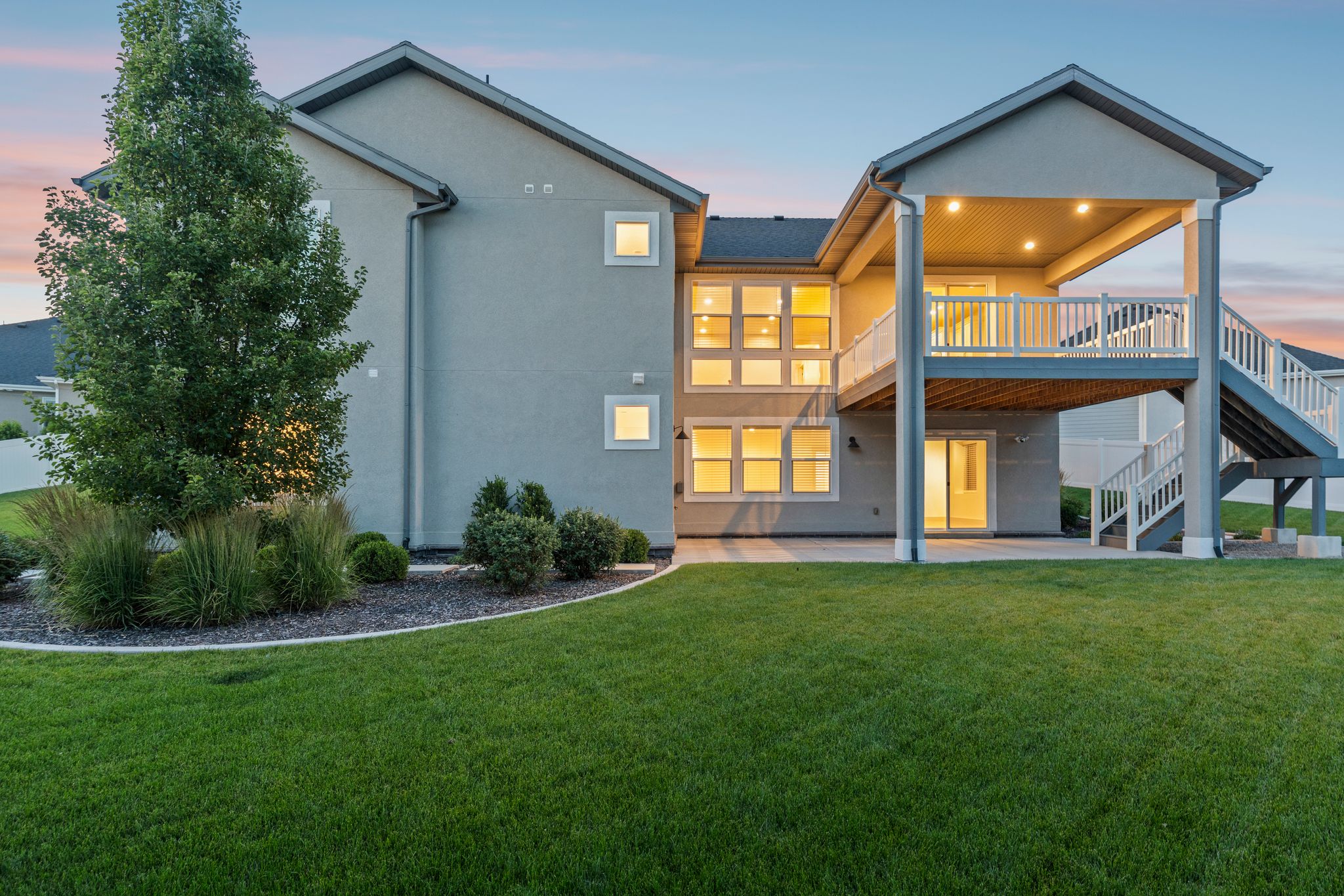 Spacious rear exterior featuring a covered deck, lower patio, and a manicured lawn