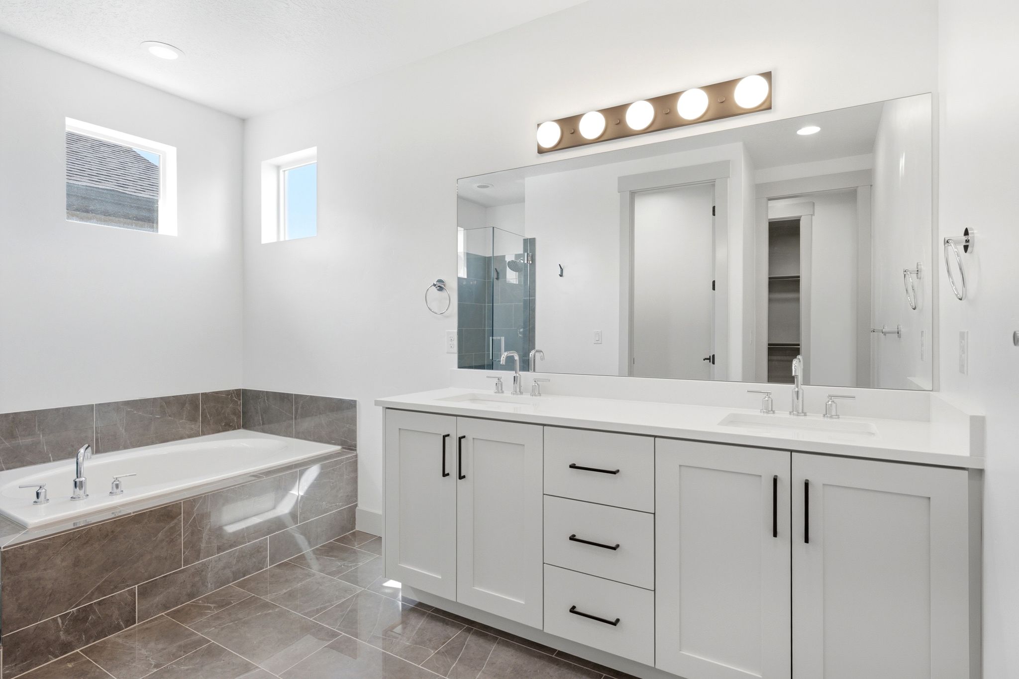 Bathroom featuring a dual vanity with white cabinetry, matte black hardware, and an expansive mirror with overhead lighting